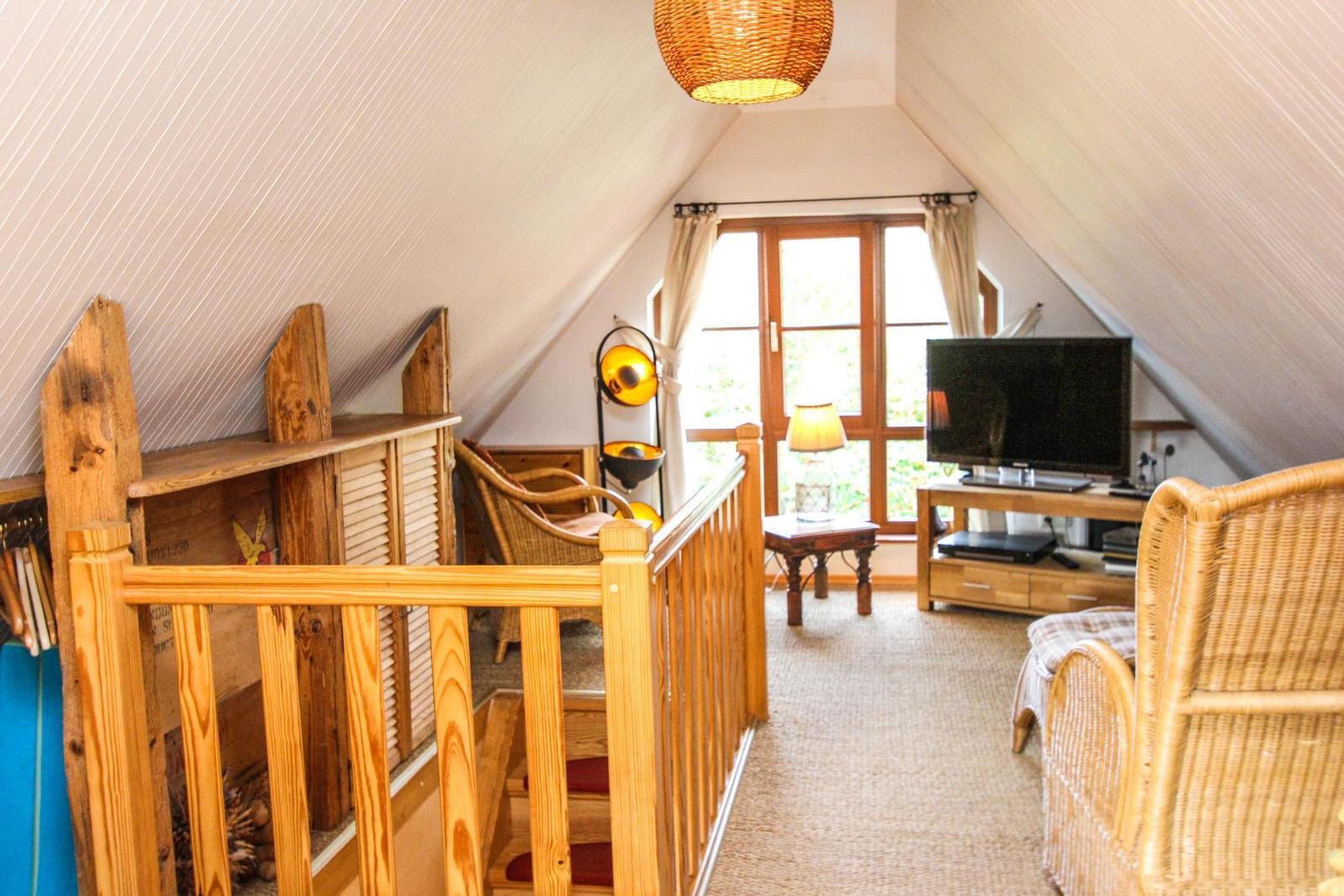 Dachgeschosszimmer mit Holzgeländer, TV und Fenster zum Garten.