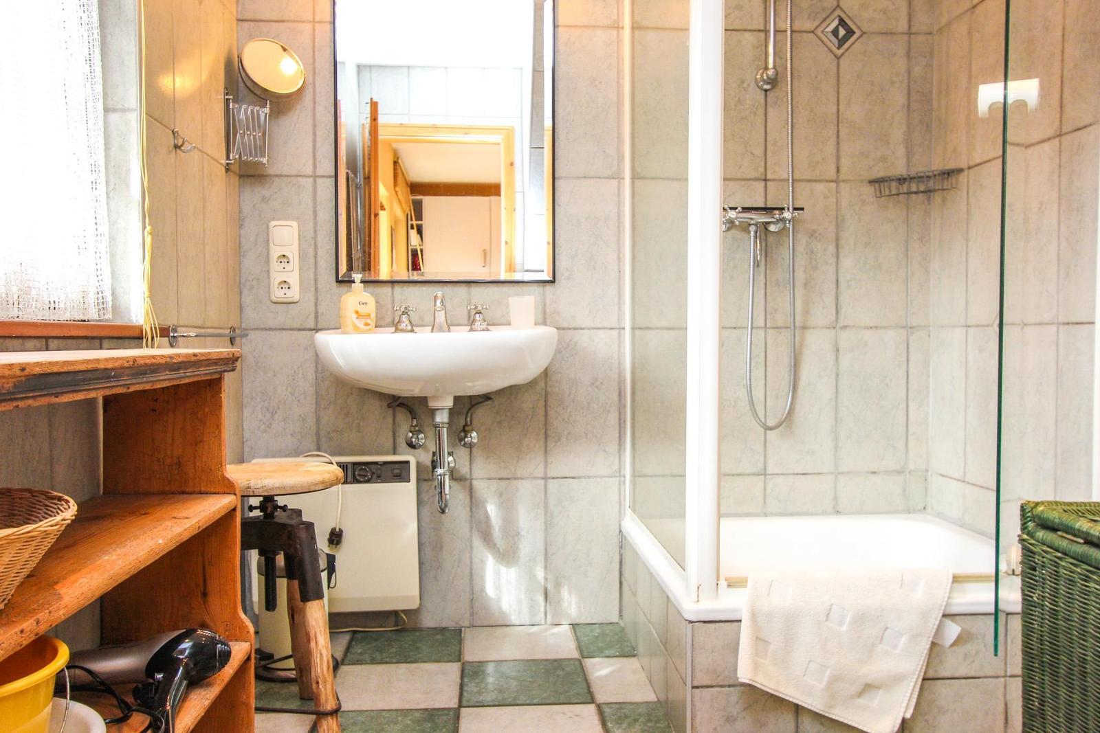 Badezimmer mit Dusche, Waschbecken und Holzregal.