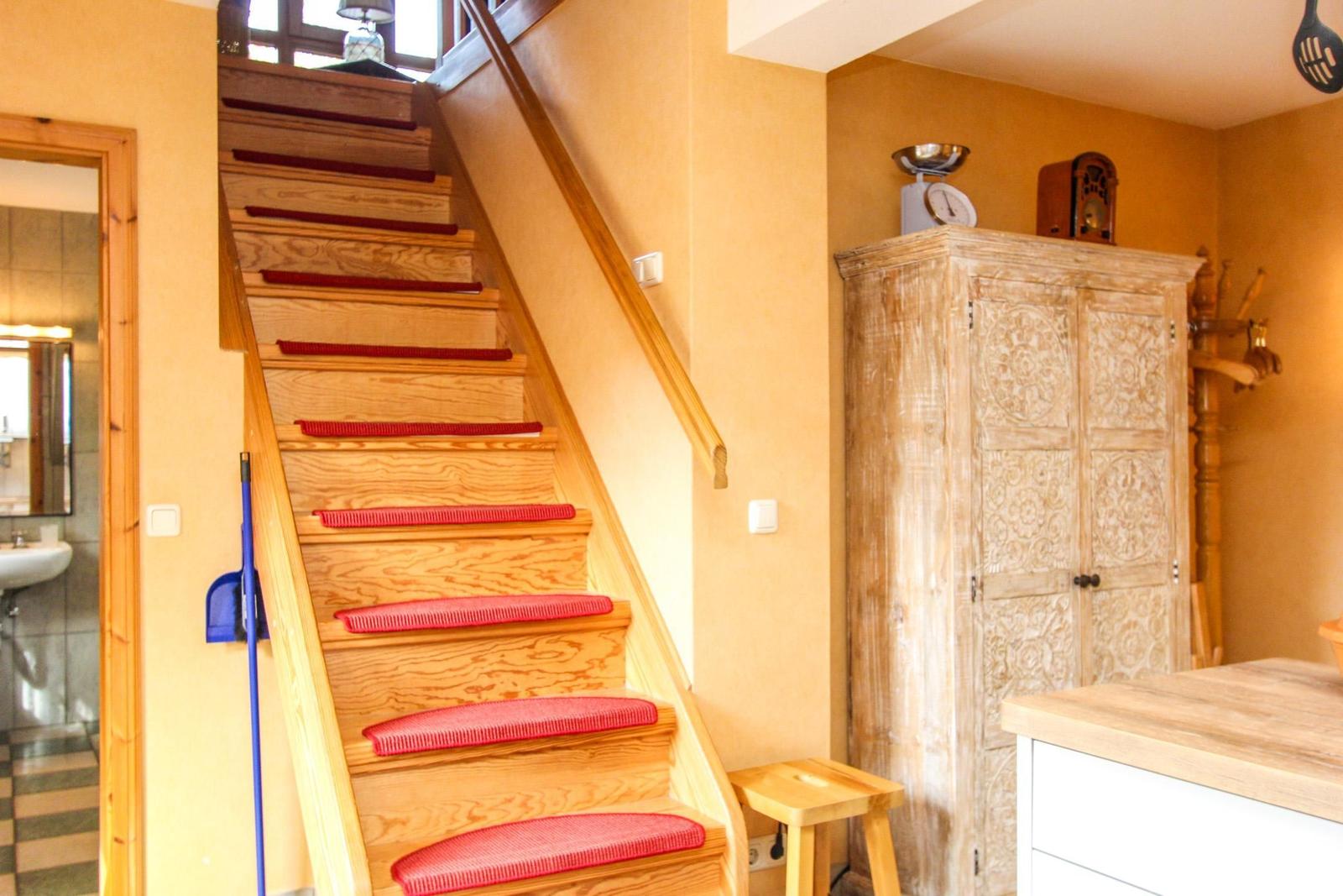 Holztreppe mit roten Matten führt zur oberen Etage. Neben einem Schrank und Küchenarbeitsplatte.
