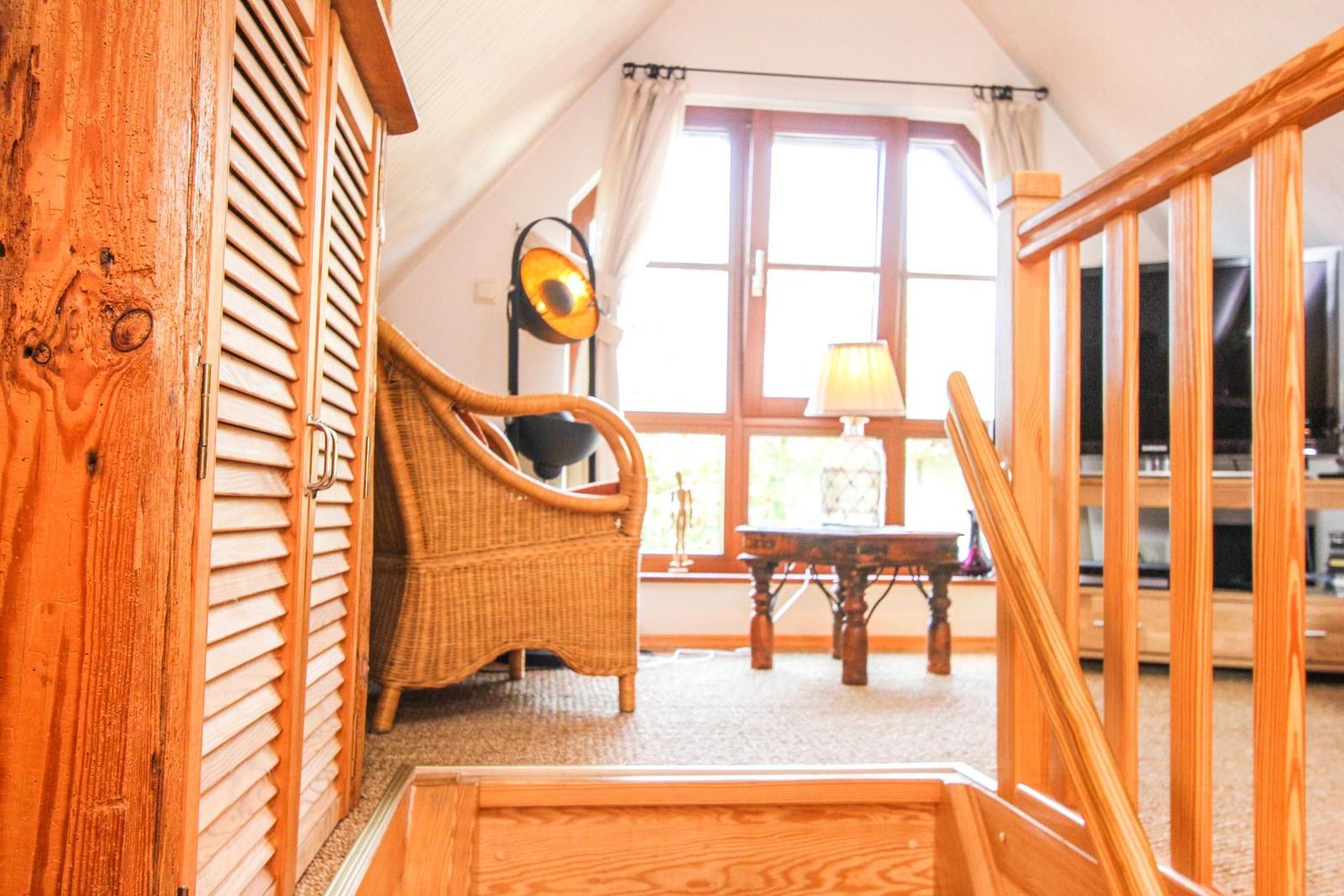 Durchgang in ein Zimmer mit Holzgeländer, Wickerstuhl und Fenster.