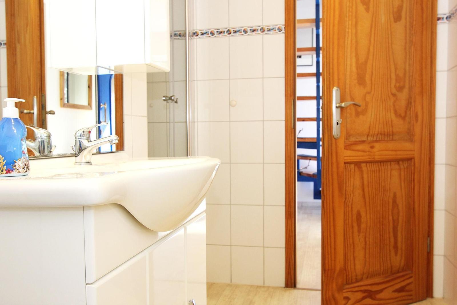 Bad mit Waschbecken, Spiegel und Holztür. Durchgang zu einem Raum mit Holzstufen.