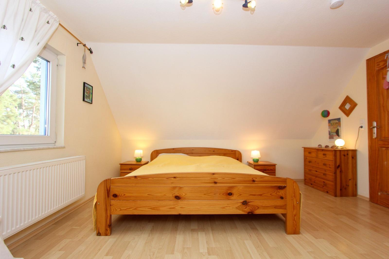 Schlafzimmer mit Holzbett, Nachttischen und Schrank. Fenster mit Blick auf Wald.