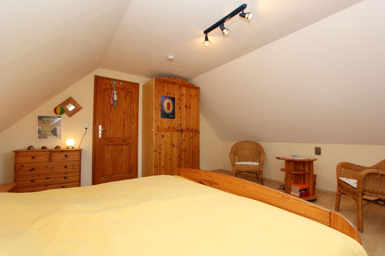 Schlafzimmer mit Holzbett, Kleiderschrank und Stuhl. Dachschrägen und Holzmöbel.