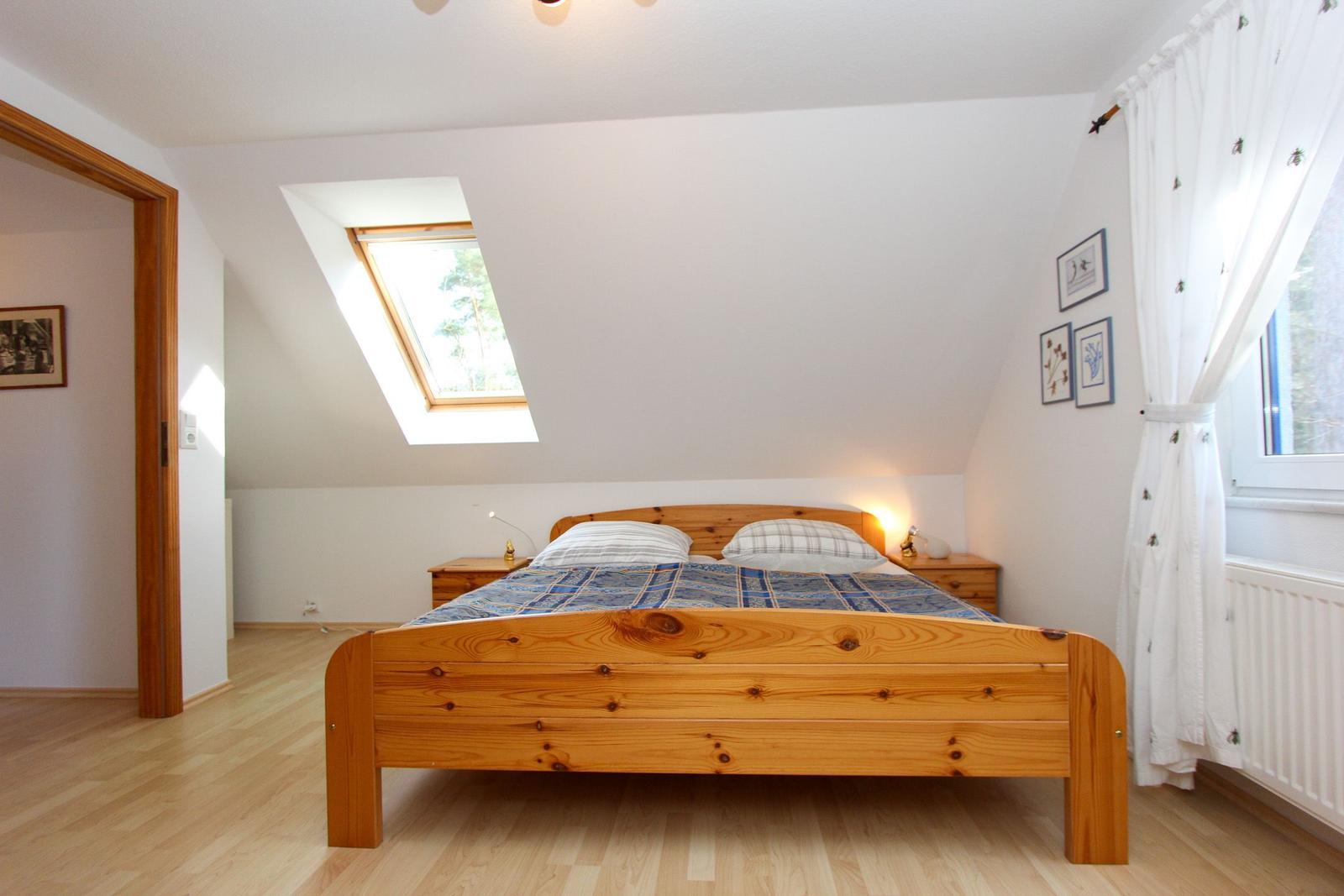 Schlafzimmer mit Holzbett, Dachfenster und weißen Wänden.