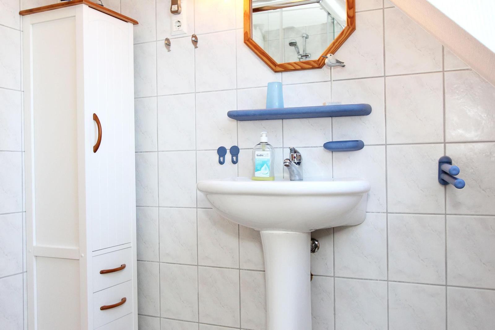 Badezimmer mit Waschbecken, Spiegel und weißen Fliesen.