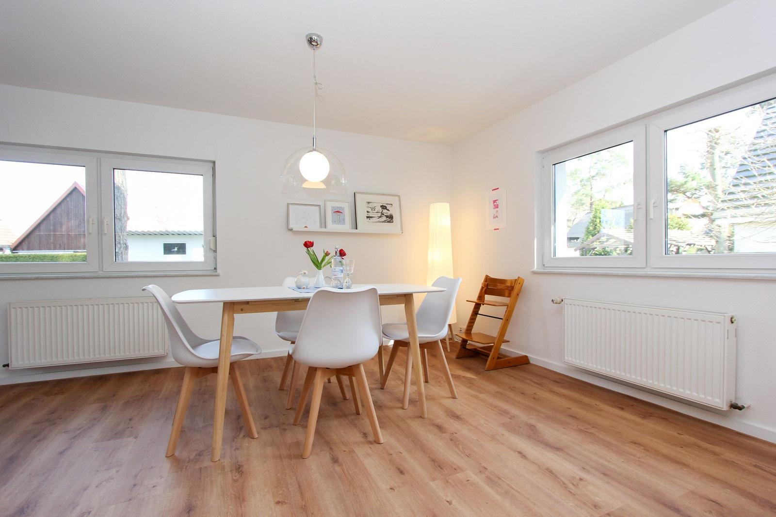 Esszimmer mit Tisch, Stühlen und Fenstern. Holzboden und weiße Wände.