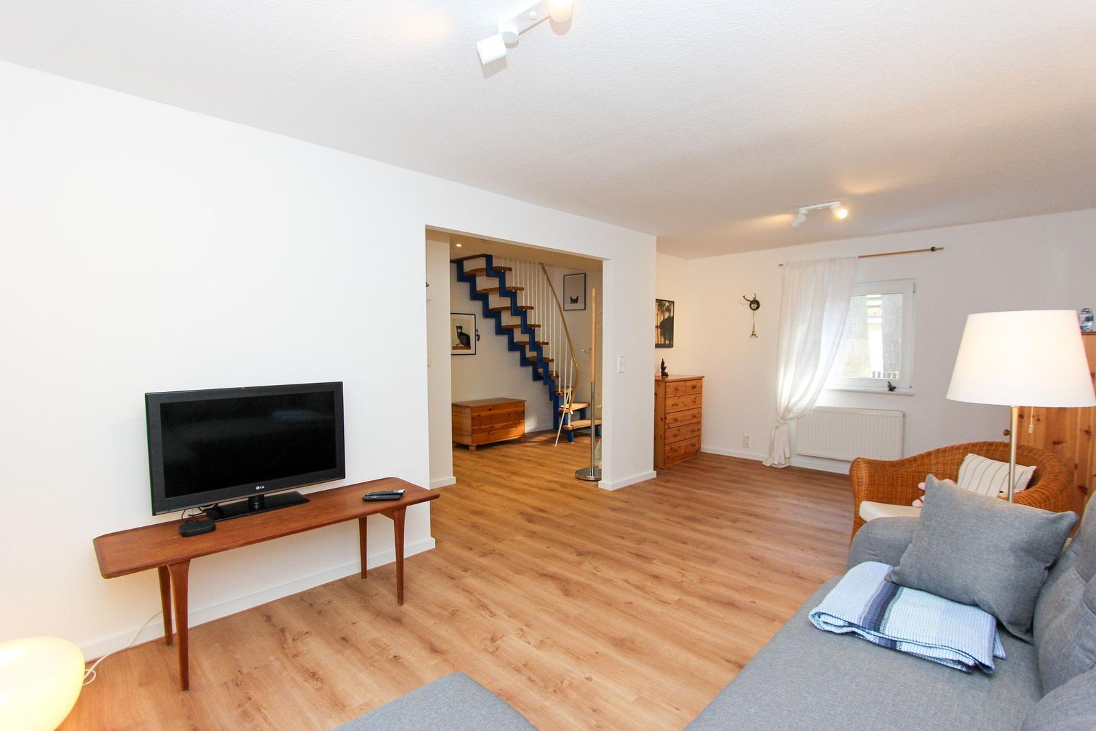Wohnzimmer mit Sofa, Fernseher und Holzboden. Treppe führt in den zweiten Stock.