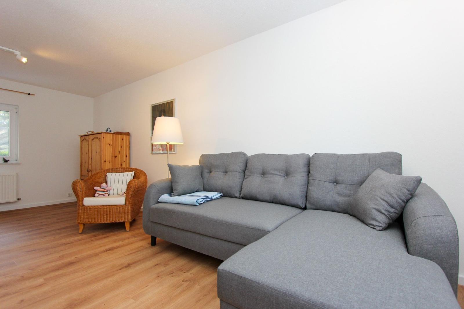 Wohnzimmer mit grauem Sofa, Holzboden und Wicker-Sessel.