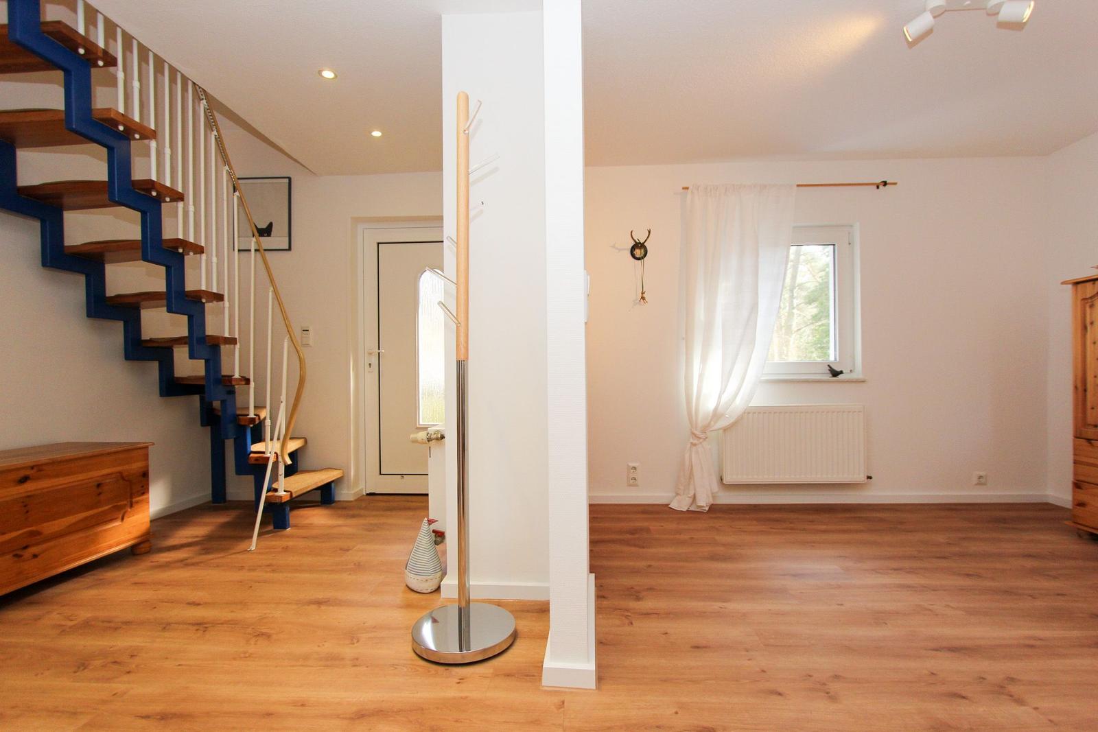 Eingangsbereich mit Holzboden, Treppe und Garderobe. Fenster mit Vorhängen und Heizkörper.