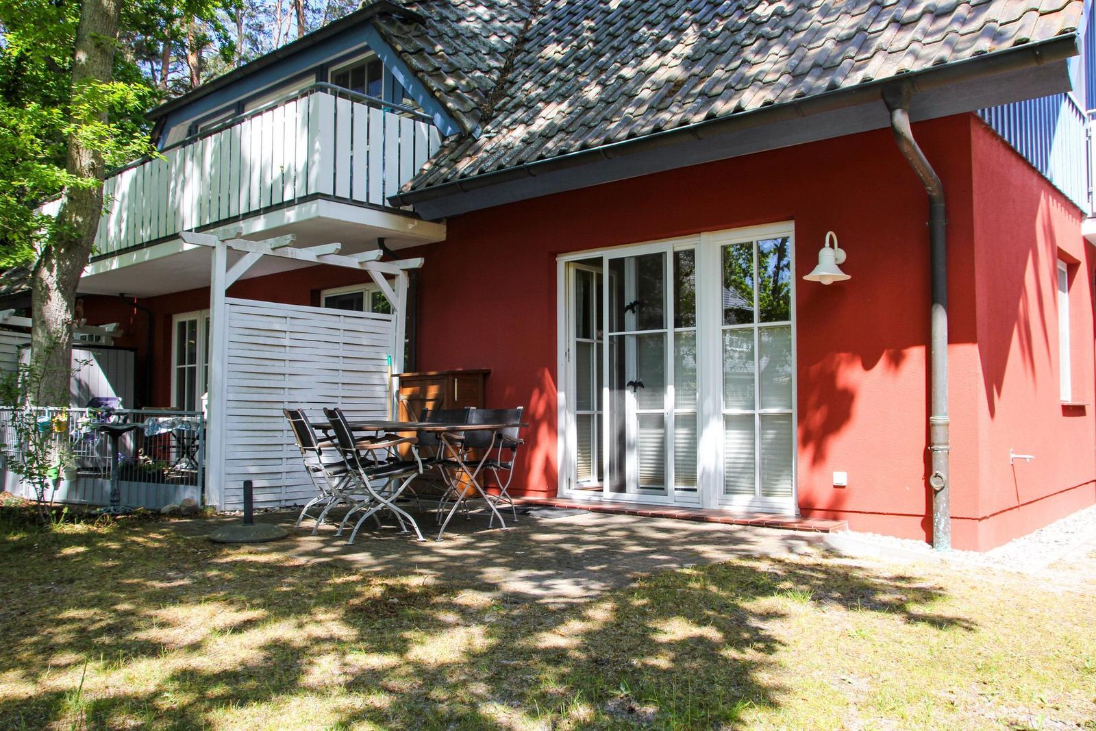 Rotes Haus mit Terrasse, Garten und Balkon. Glastüren führen ins Innere.
