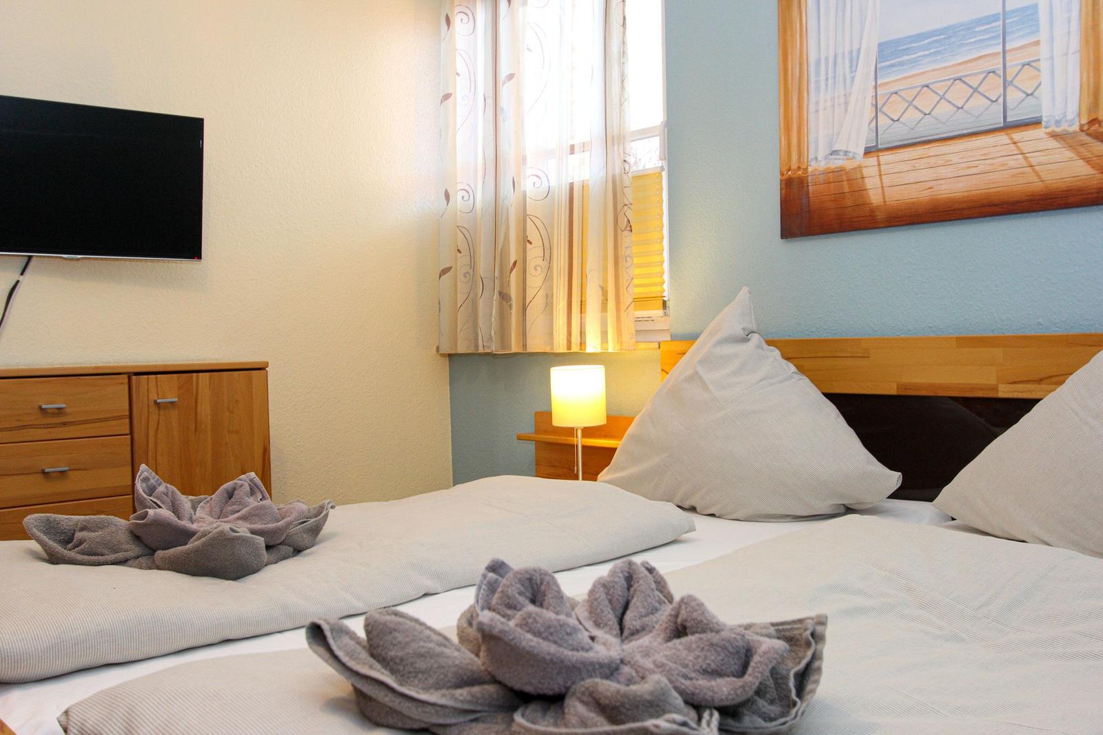 Schlafzimmer mit Bett, Fernseher und Fenster mit Blick auf Strand.