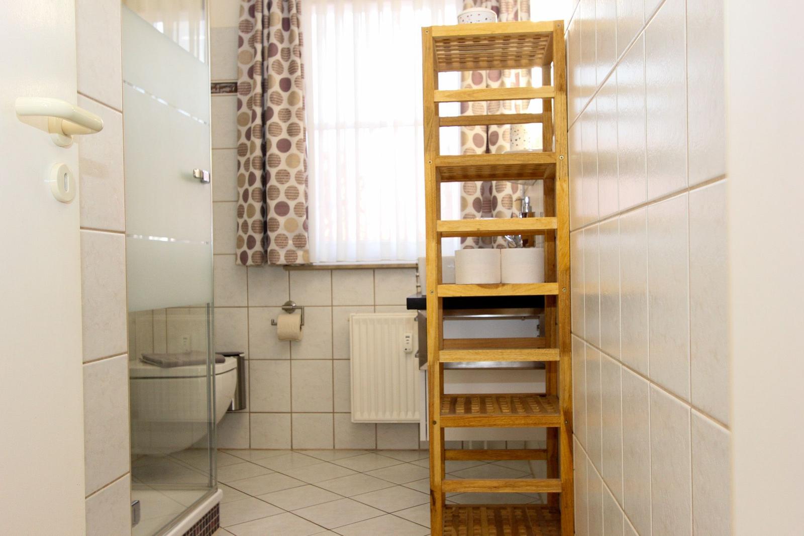 Badezimmer mit Dusche, Toilette und hölzernem Regal.