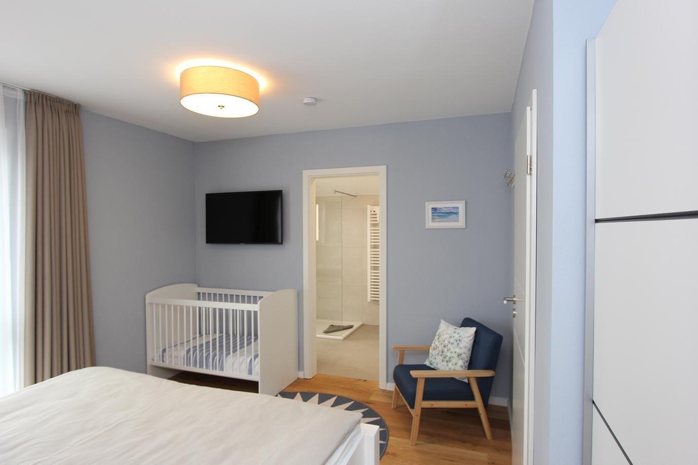 Schlafzimmer mit Babybett, Fernseher und Blick in die Dusche.