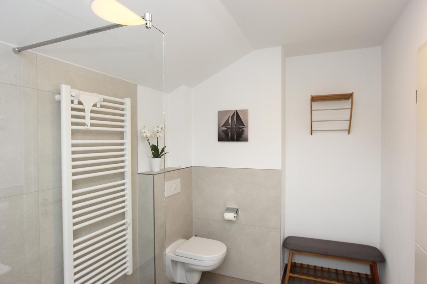 Badezimmer mit Dusche, Toilette, Heizung und Holzregal an der Wand.