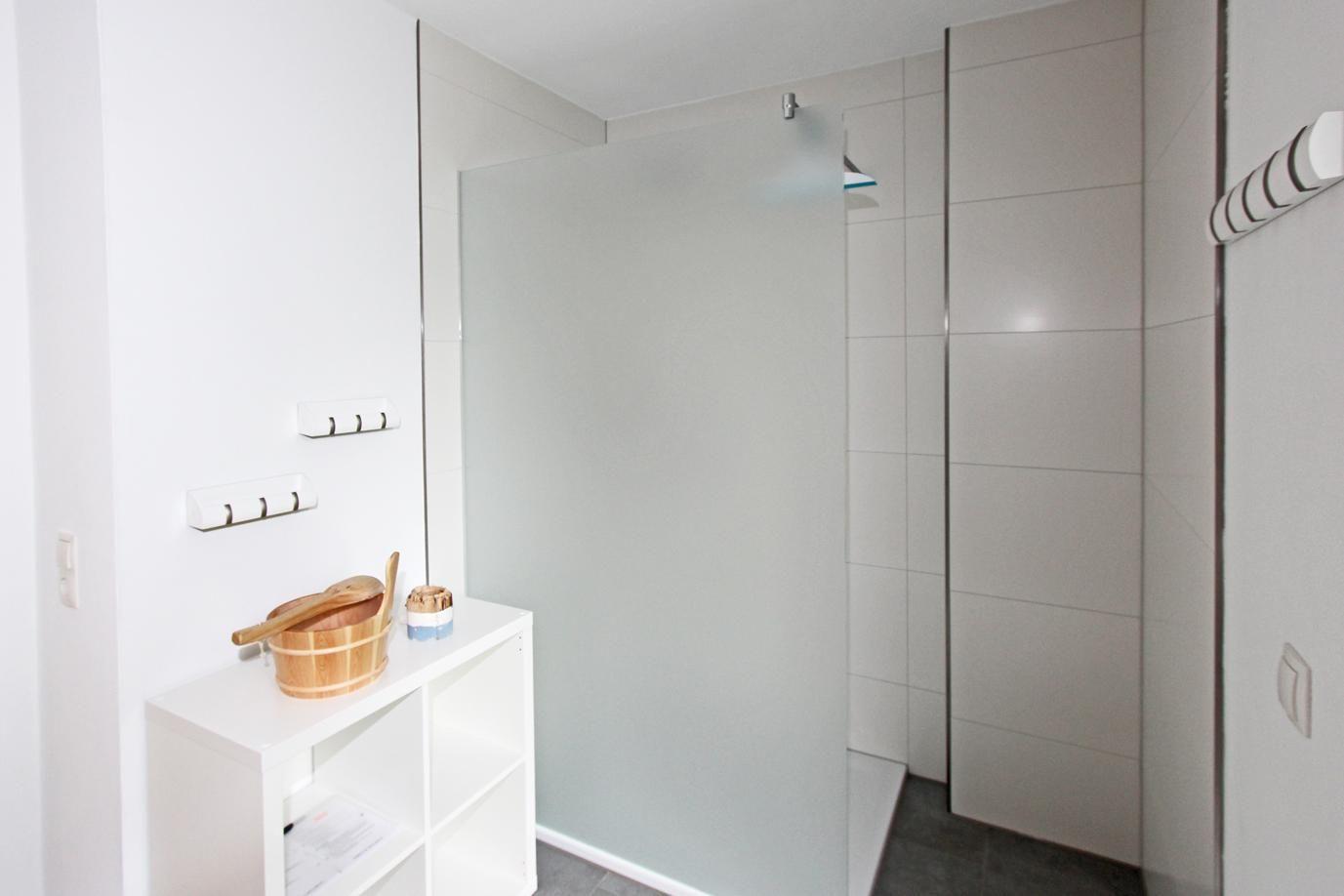 Dusche mit Glaswand, weiße Fliesen und kleiner weißer Regal mit Holzwaschschale.