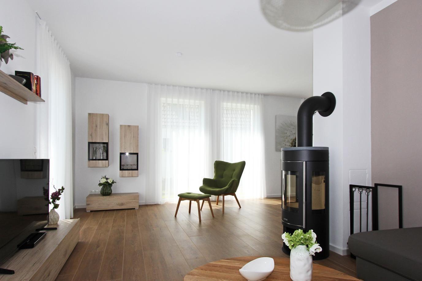 Wohnzimmer mit Holzboden, grüner Sessel, Kaminofen und großem Fenster
