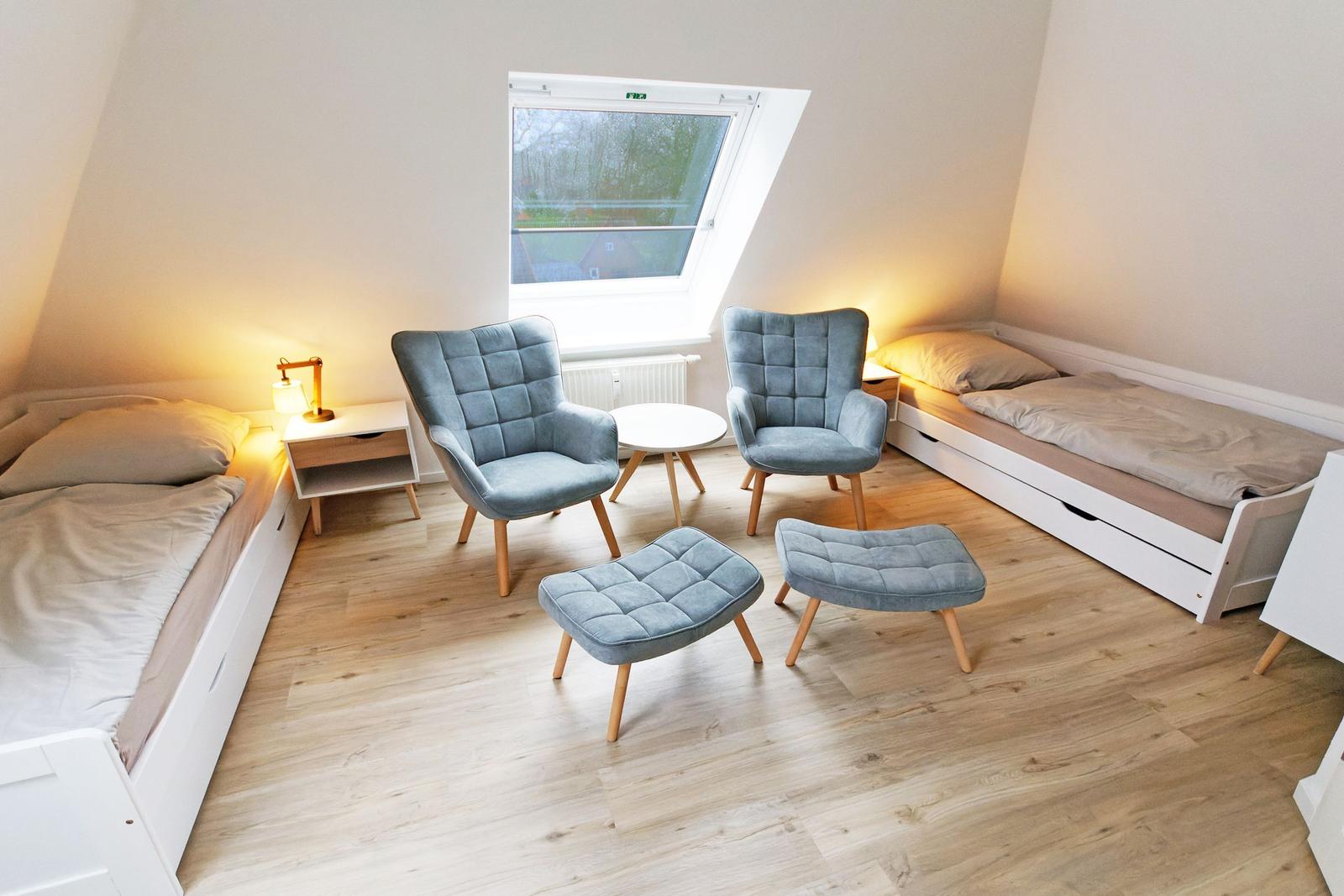 Zimmer mit zwei Betten, zwei Sesseln und einem Fenster