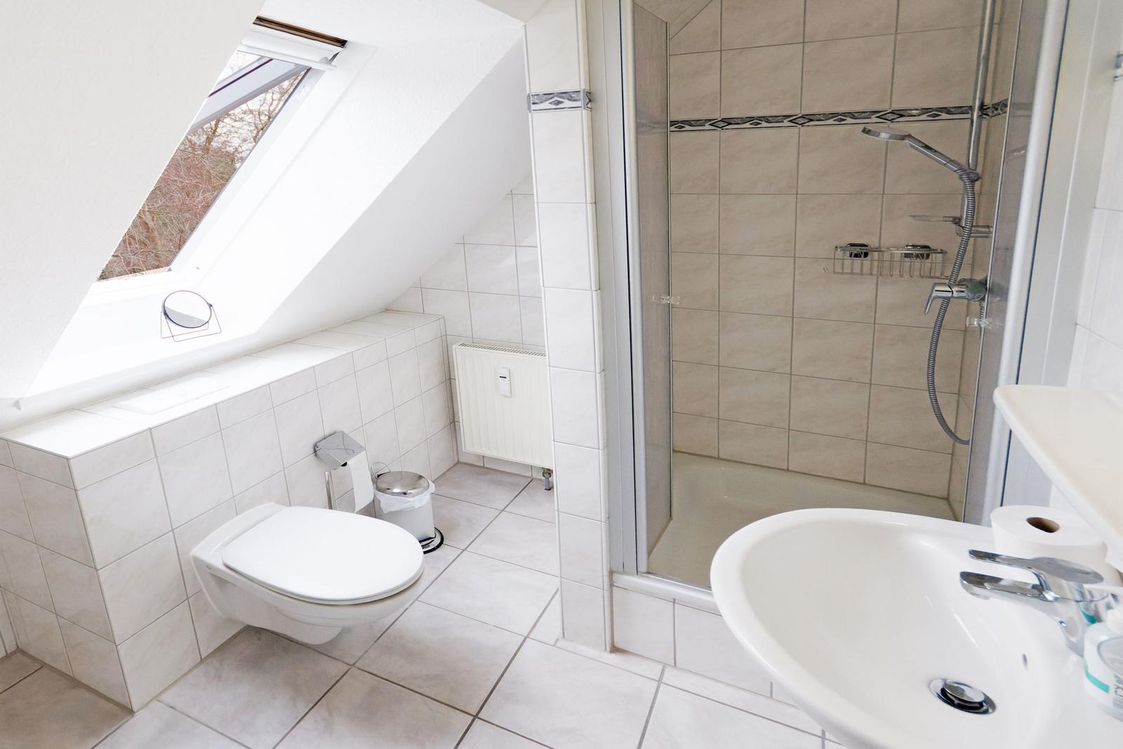 Badezimmer mit Dusche, Toilette und Waschbecken unter Dachschräge mit Fenster.