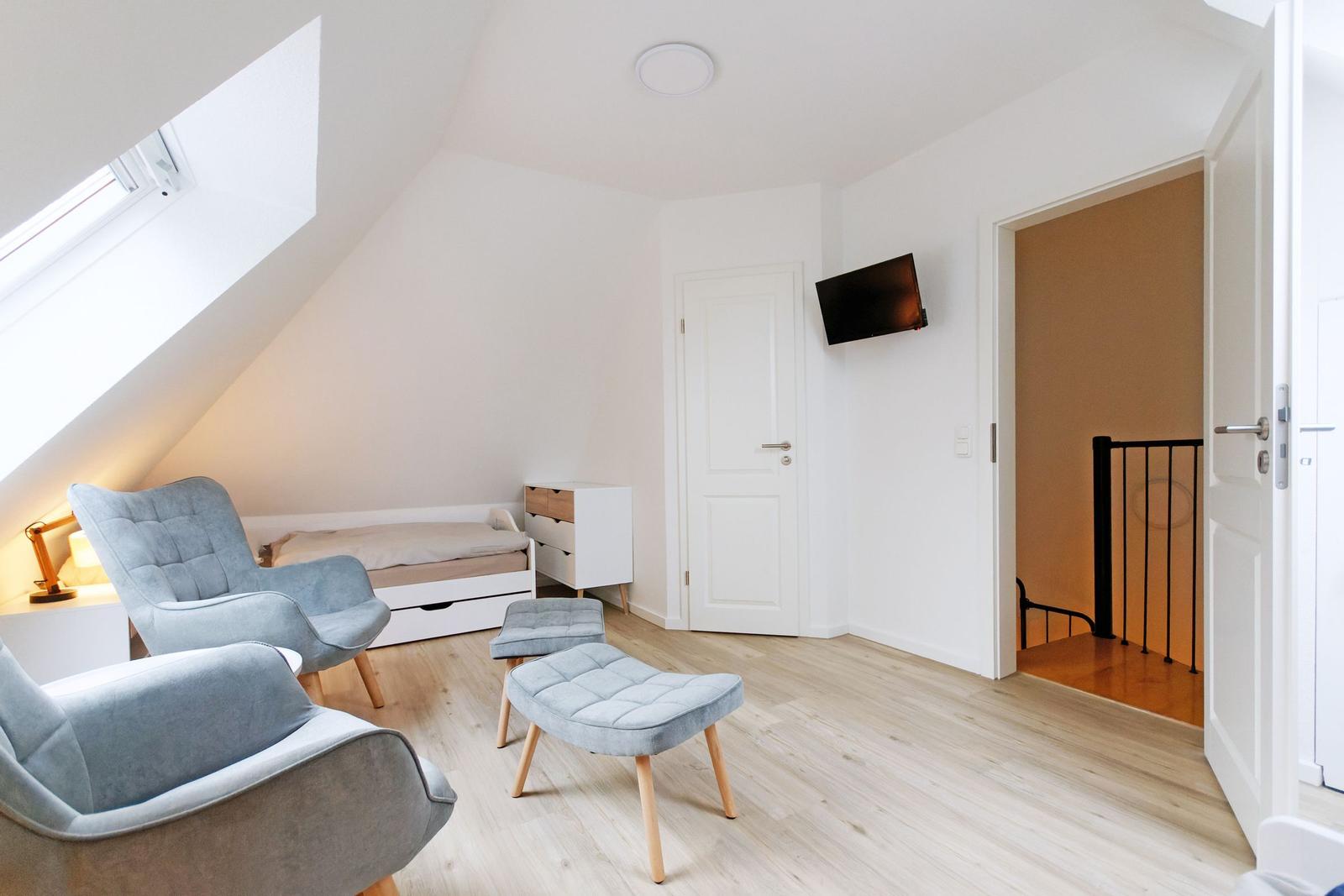 Schlafzimmer mit Dachschrägen, Bett, zwei Sesseln und Fernseher an der Wand.
