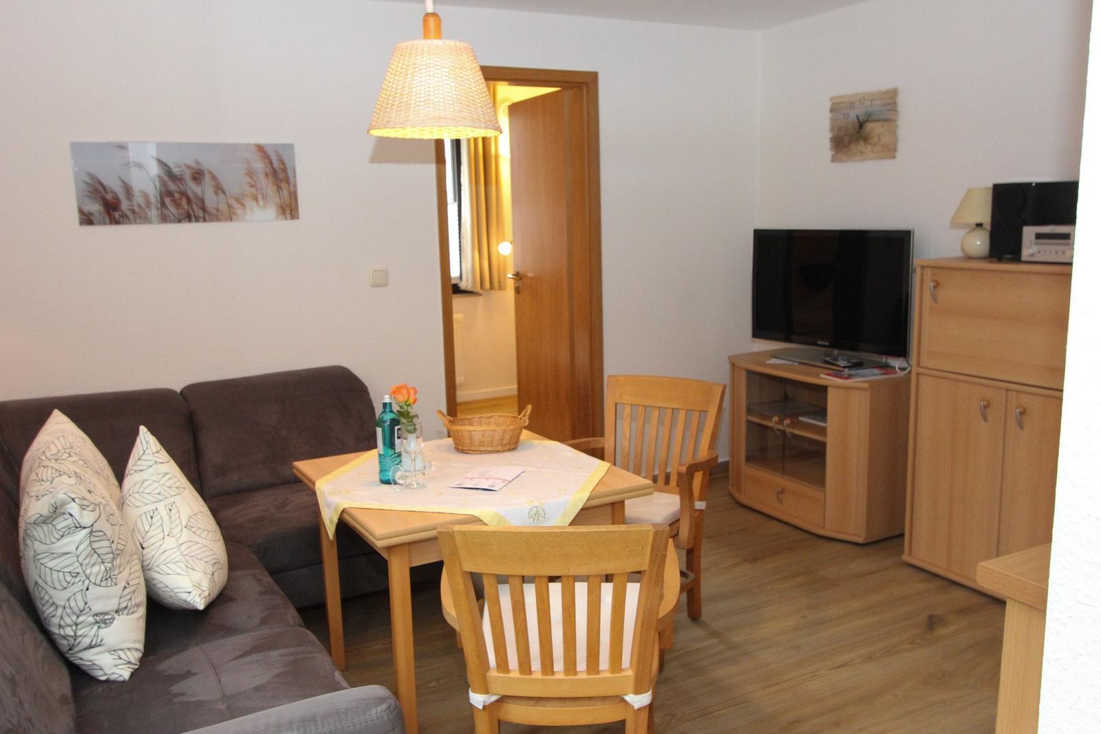 Wohnzimmer mit Sofa, Esstisch und Fernseher. Holzmöbel und Wandbild.