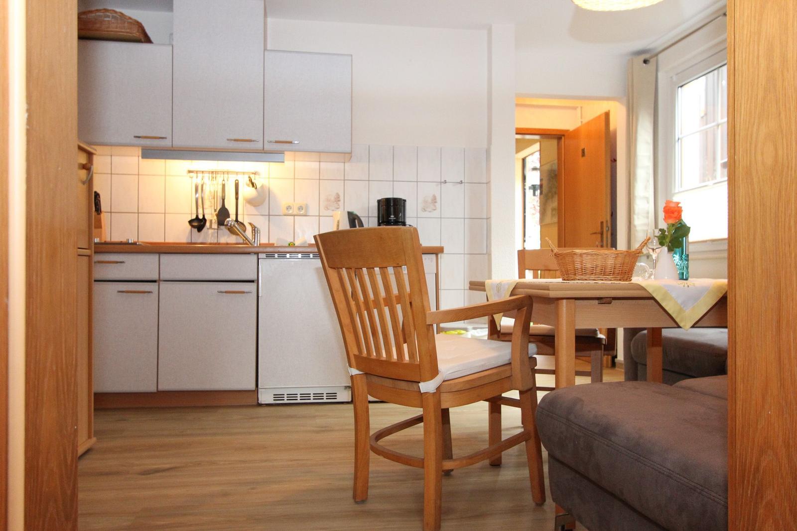 Küche mit Essbereich, Holzmöbel und Fenster. Weiße Schränke und Fliesenwand.