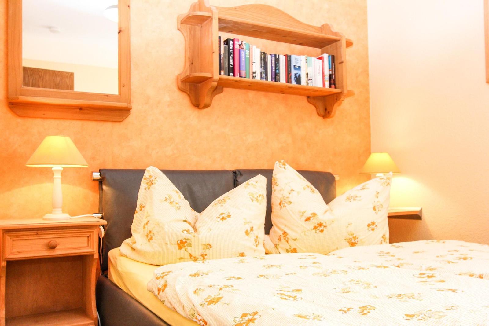 Schlafzimmer mit Bett, Nachttischen und Bücherregal an der Wand.