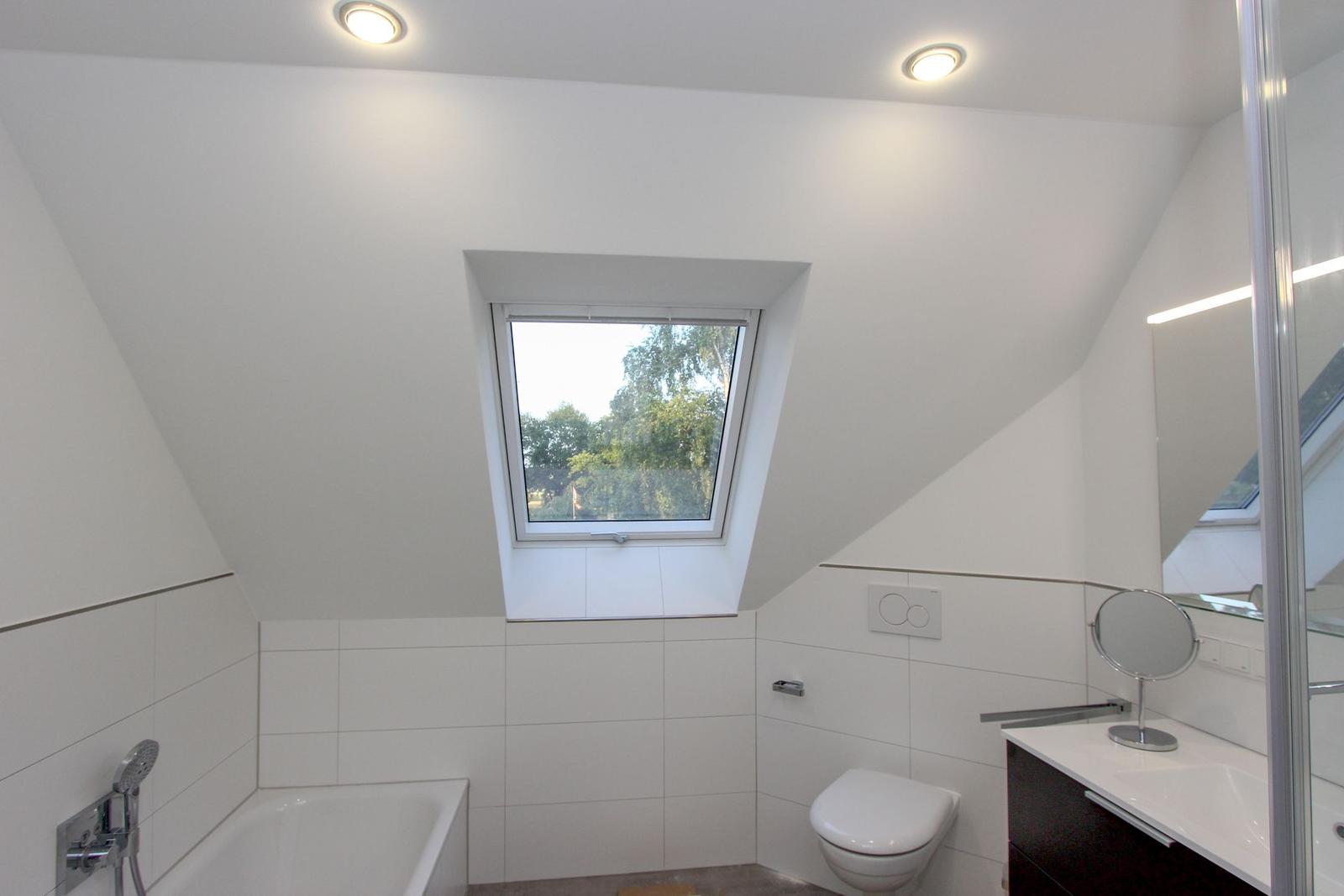 Badezimmer mit Dachfenster, Badewanne, Toilette und Waschbecken.