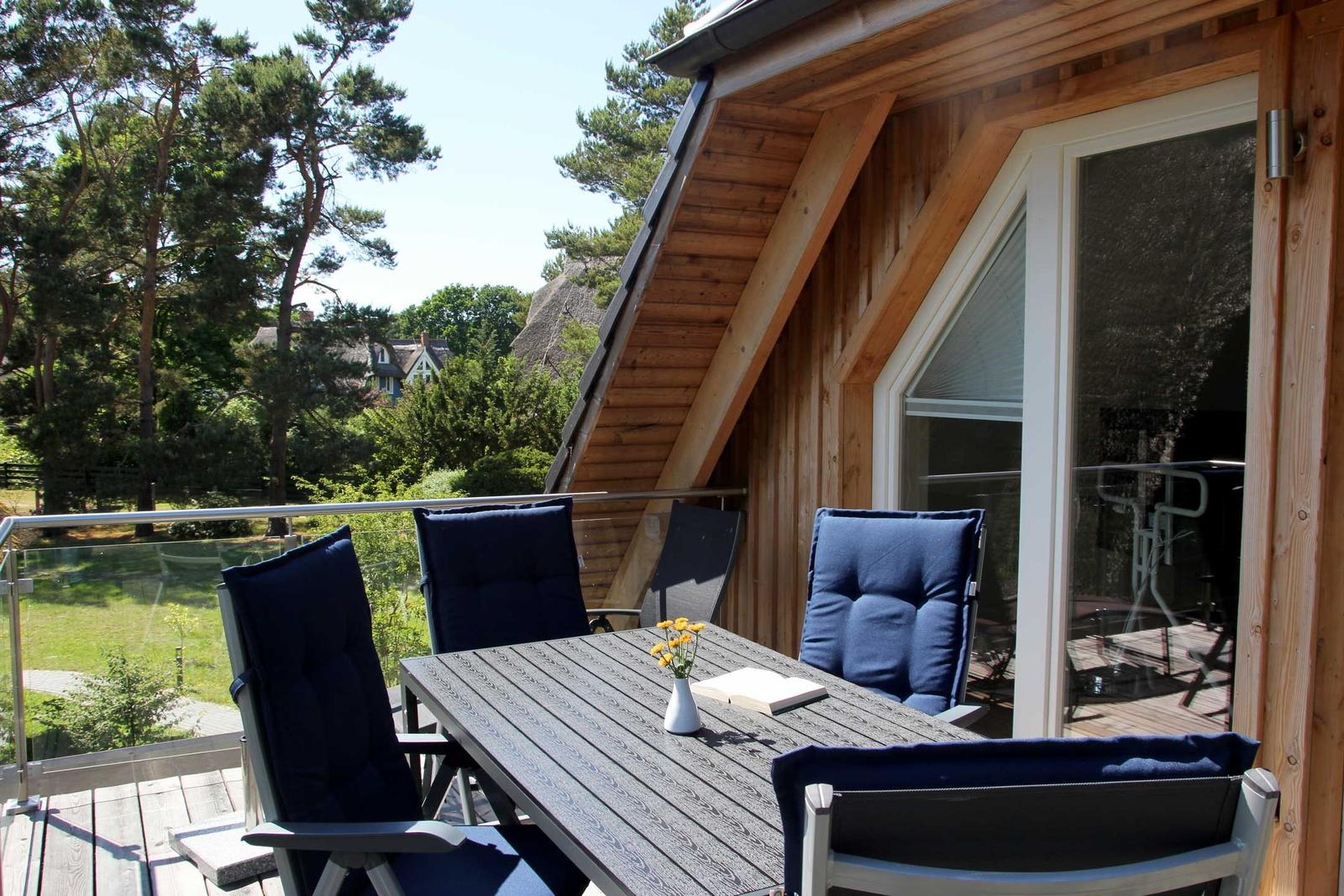 Terrasse mit Tisch und Stühlen, Blick auf Wald und Häuser.