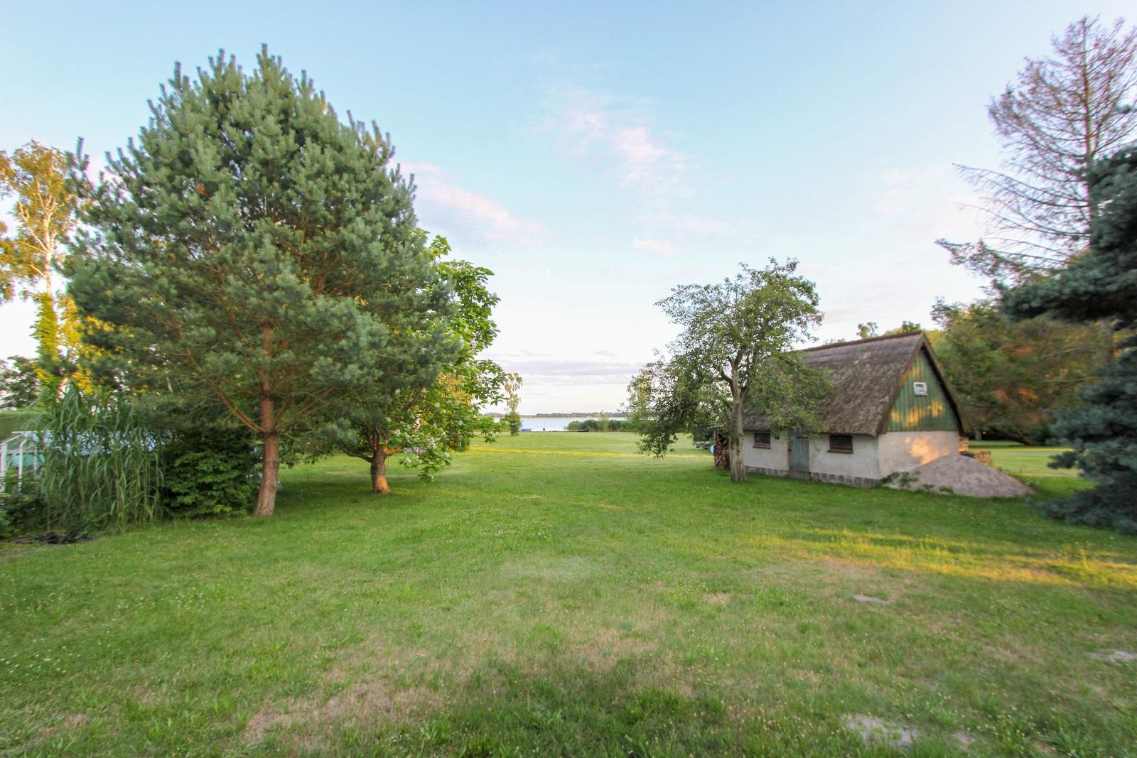 Ein kleines Haus mit Schopfdecke steht auf einer grünen Wiese neben einem See.