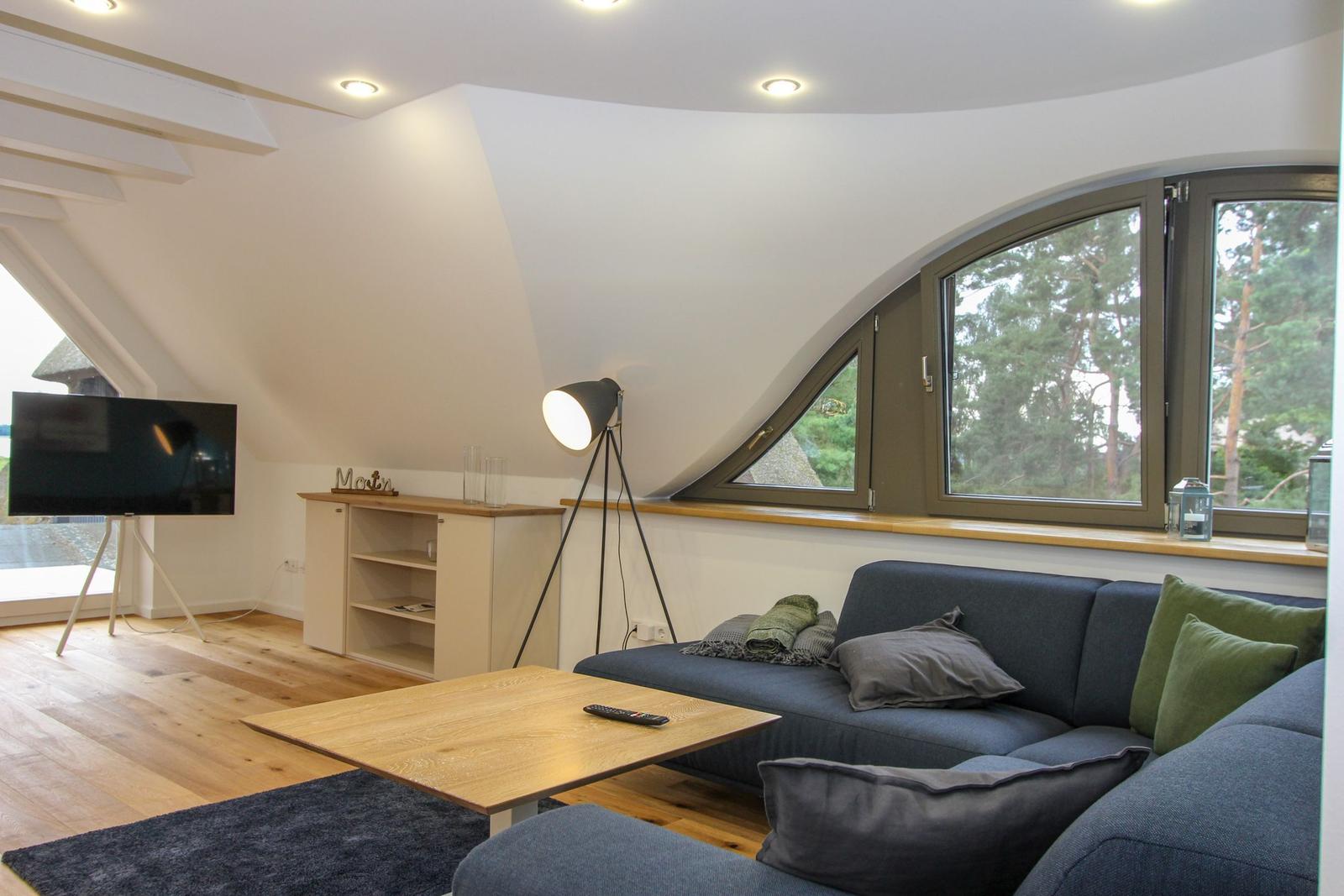 Wohnzimmer mit Sofa, Couchtisch und TV unter schrägen Dachfenstern.