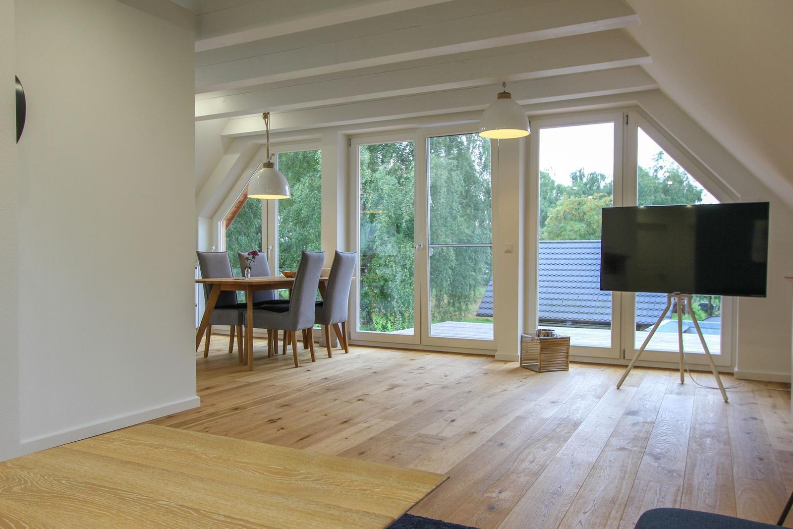 Wohnbereich mit Essbereich, Holzboden und großem Fenster. Fernseher auf Stativ.