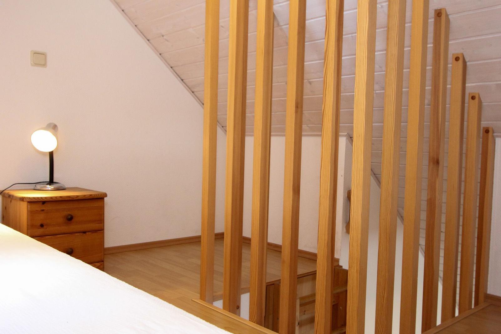 Schlafzimmer mit Holzbalken, Nachttisch und Lampe unter schrägem Dach