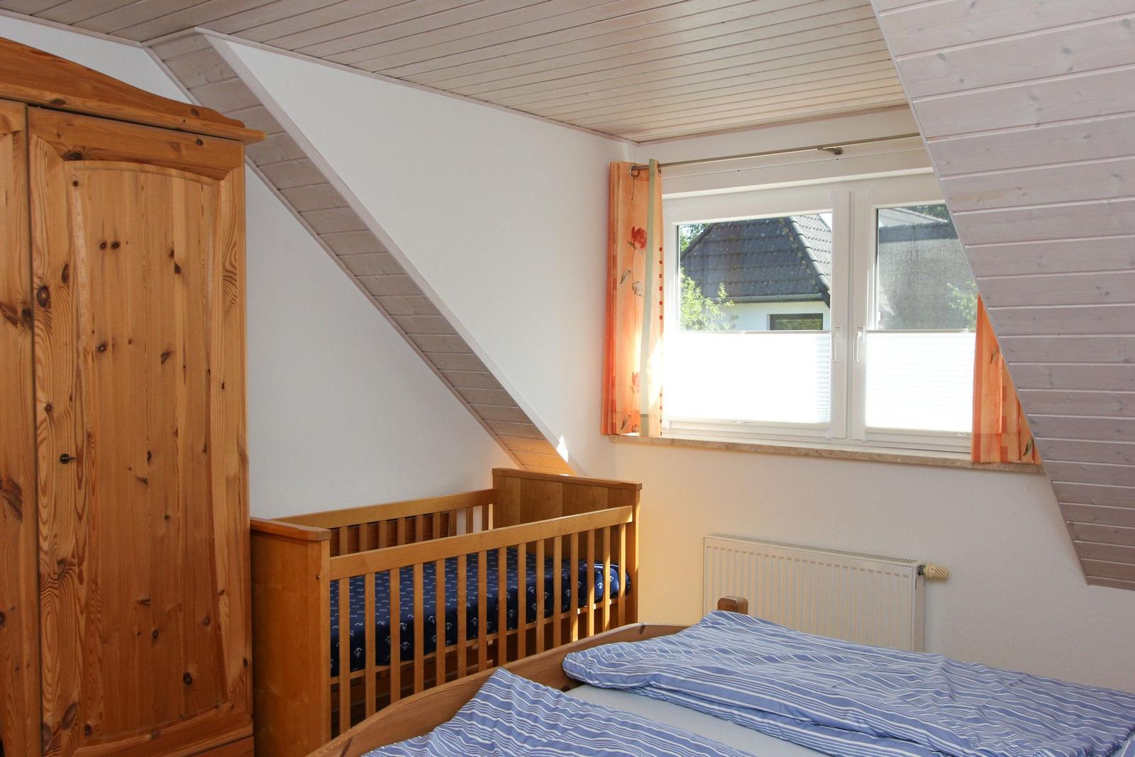 Schlafzimmer mit Babybett, Bett und Holzschrank unter Dachschräge mit Fenster.