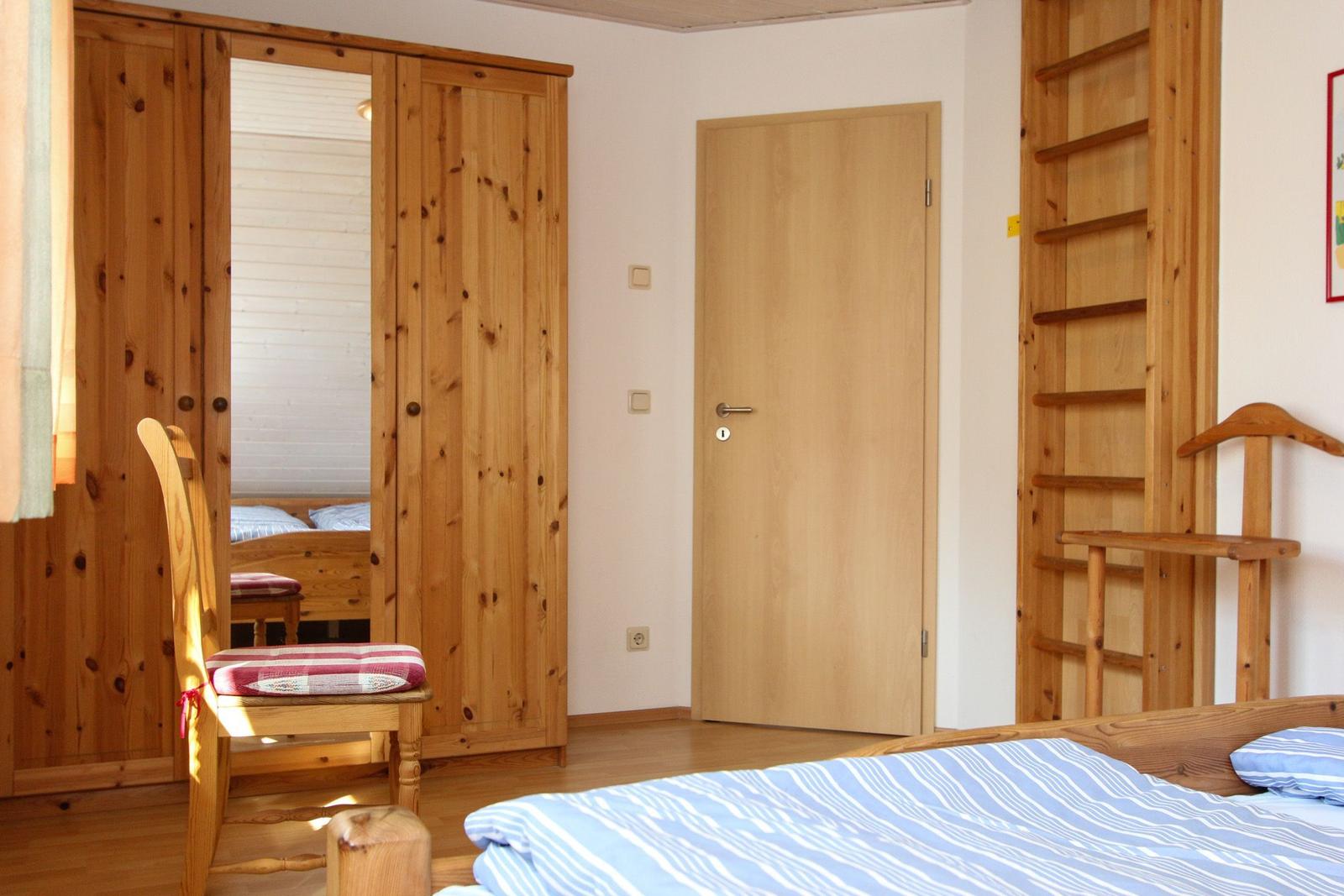 Schlafzimmer mit Holzmöbeln, Bett und Kleiderschrank. Tür und Leiter sichtbar.
