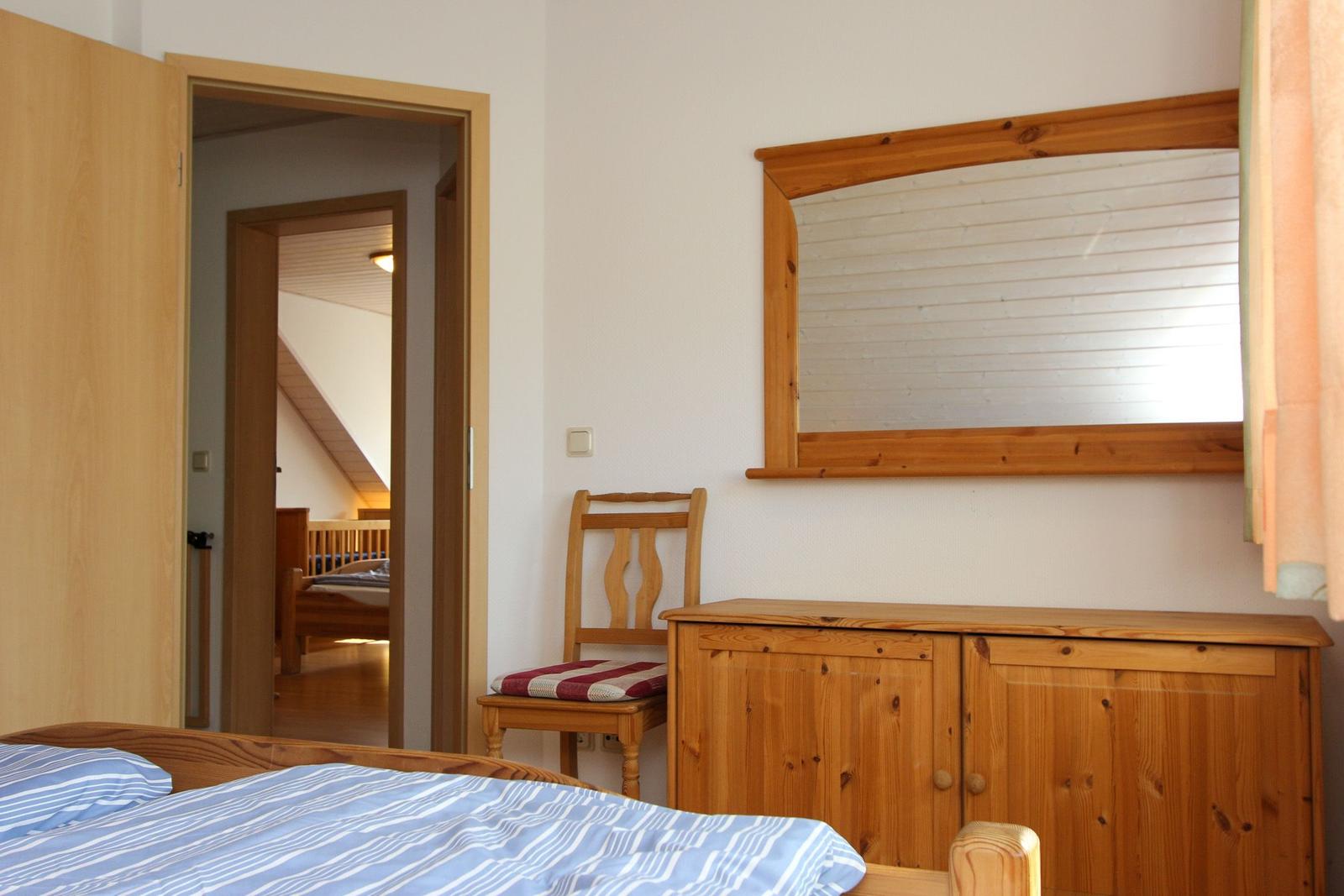 Schlafzimmer mit Holzmöbeln und Spiegel. Durchgang zu einem weiteren Raum mit Bett.