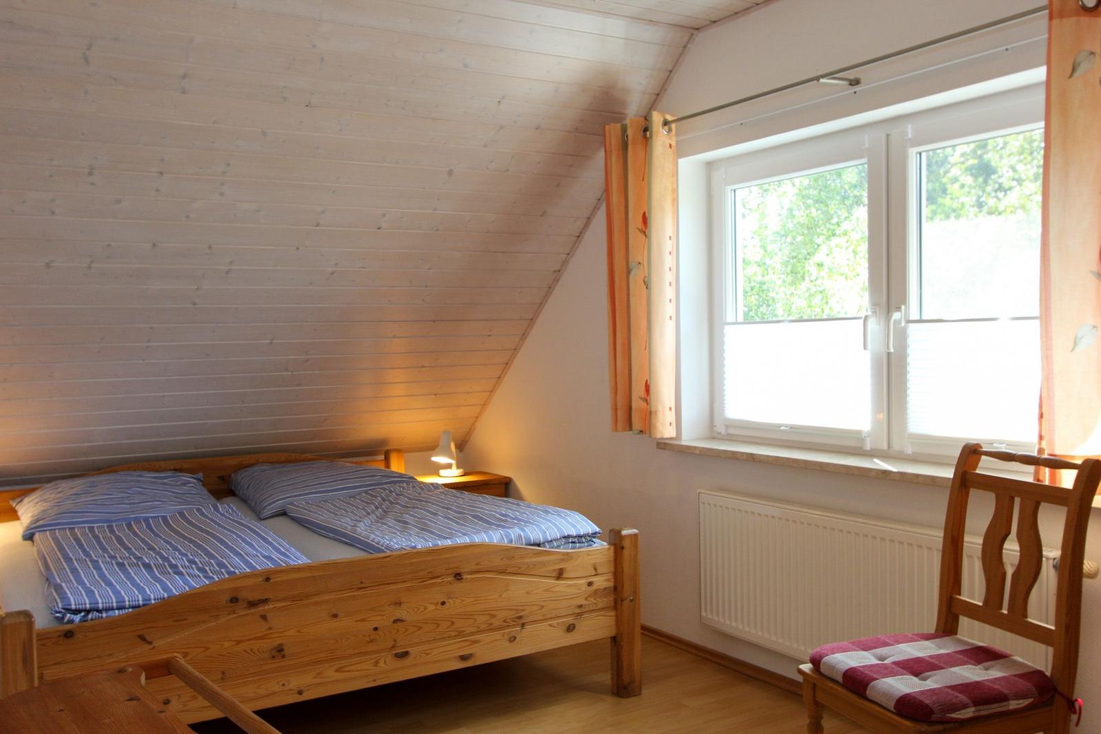 Schlafzimmer mit Holzbett, Fenster und Stuhl.