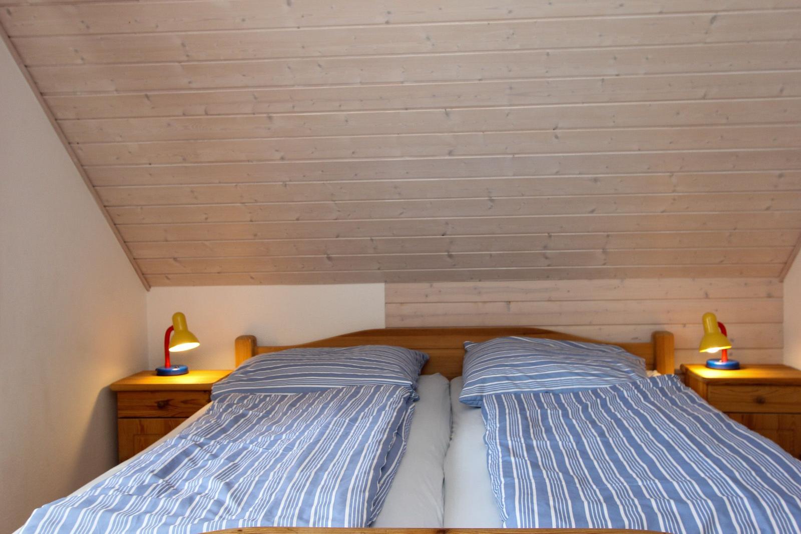 Doppelbett mit Streifenbezug, zwei Nachttische und Holzdecke.
