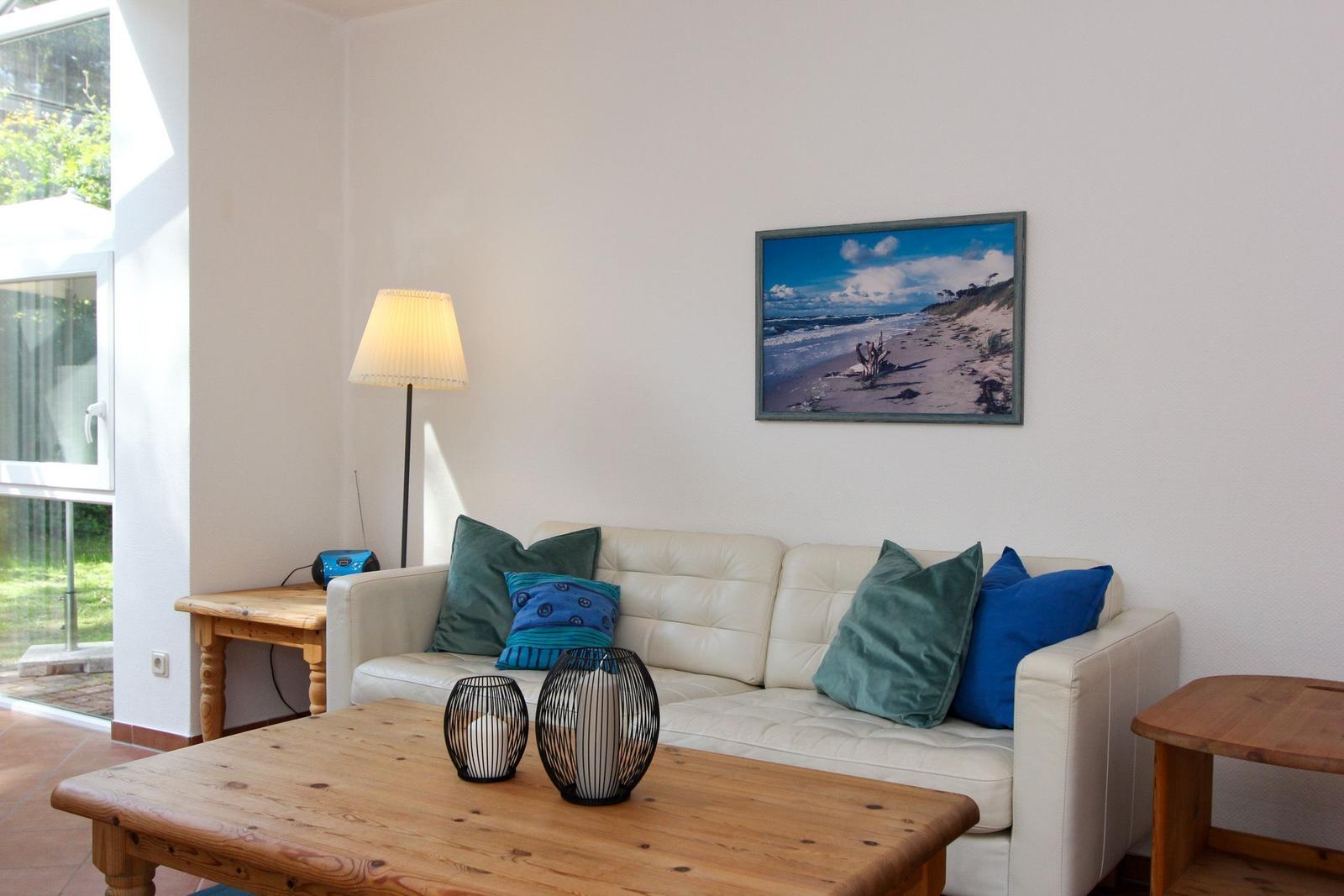 Wohnzimmer mit Sofa, Holztisch und Wandbild. Fenster mit Blick nach draußen.