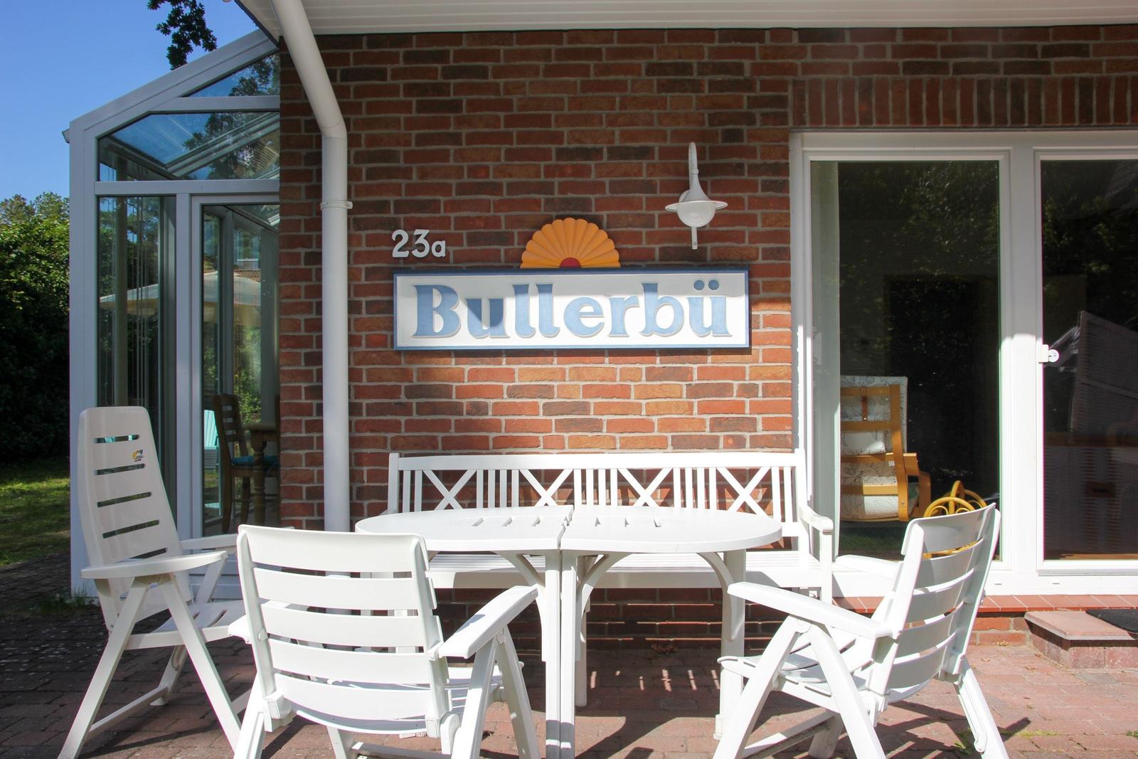 Wohnhaus mit Sitzbereich, weiße Gartenmöbel und Schild Bullerbü an rotem Ziegelsteinwand.