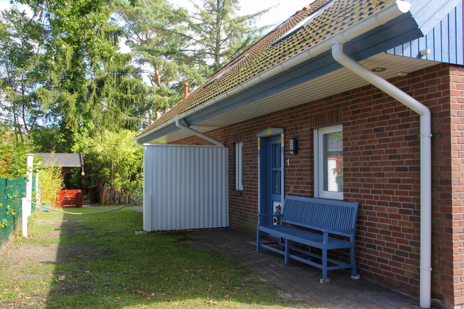Ein Haus mit Backsteinfassade, blauer Tür und Bank. Hinterhof mit Garten und Holzgarage.