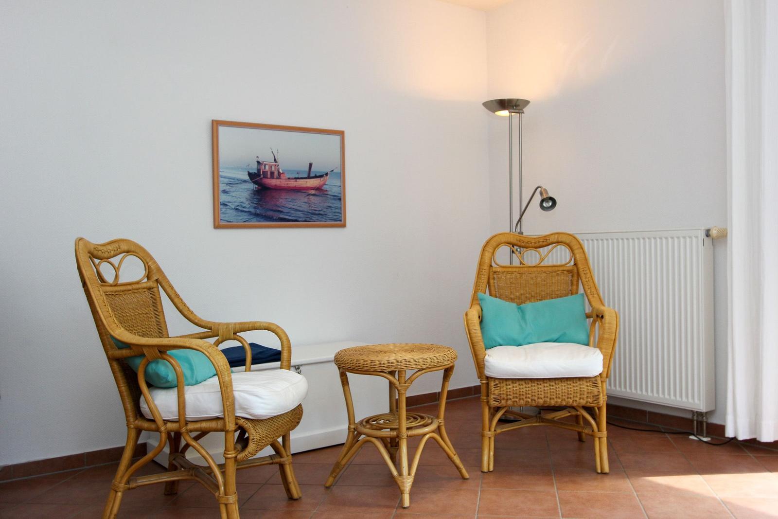 Zwei Rattan-Stühle mit Kissen, kleiner Tisch und Wandbild mit Boot.