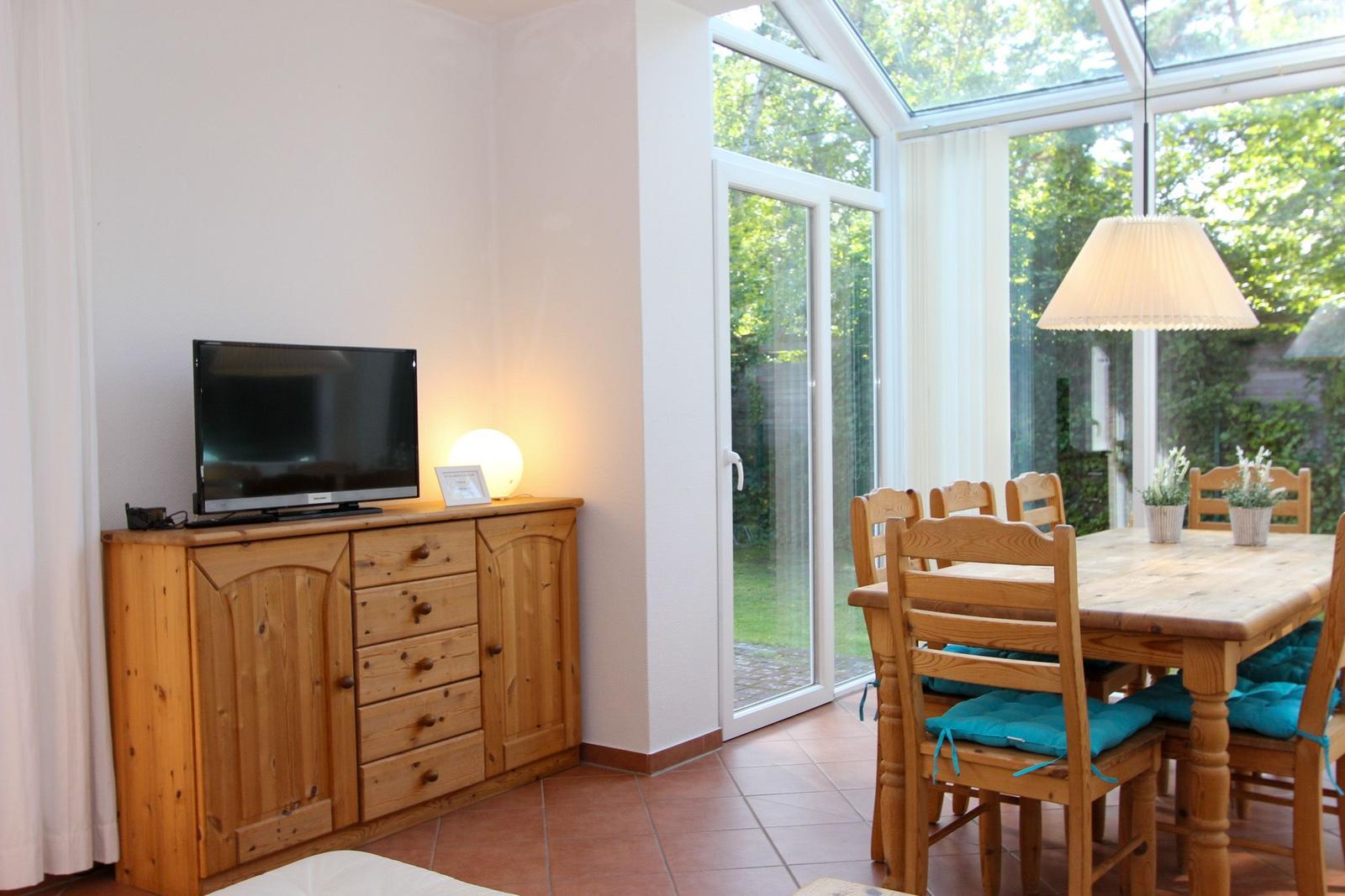 Essbereich mit Holztisch, Stühlen und Blick auf Garten. Fernseher auf Holzschrank.