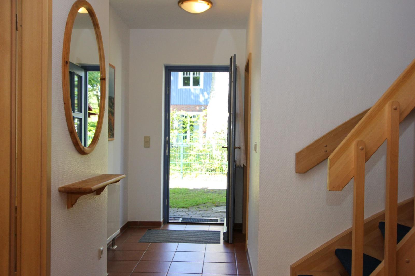 Eingangsbereich mit Holztreppe, Spiegel und offener Tür zum Garten.