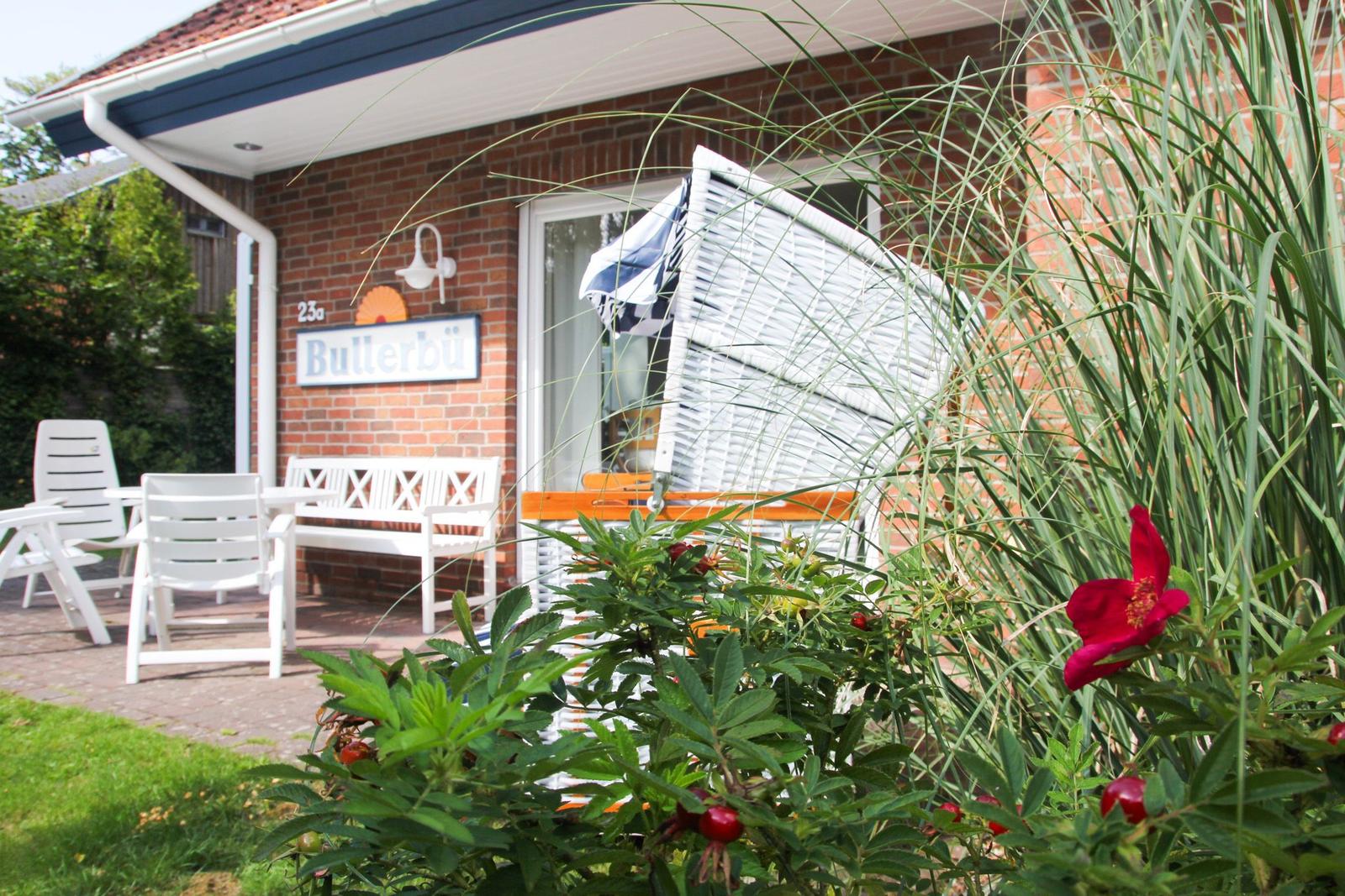 Haus mit Terrasse, weißer Bank und Gartenmöbeln. Vor dem Eingang steht ein weißer Strandkorb.