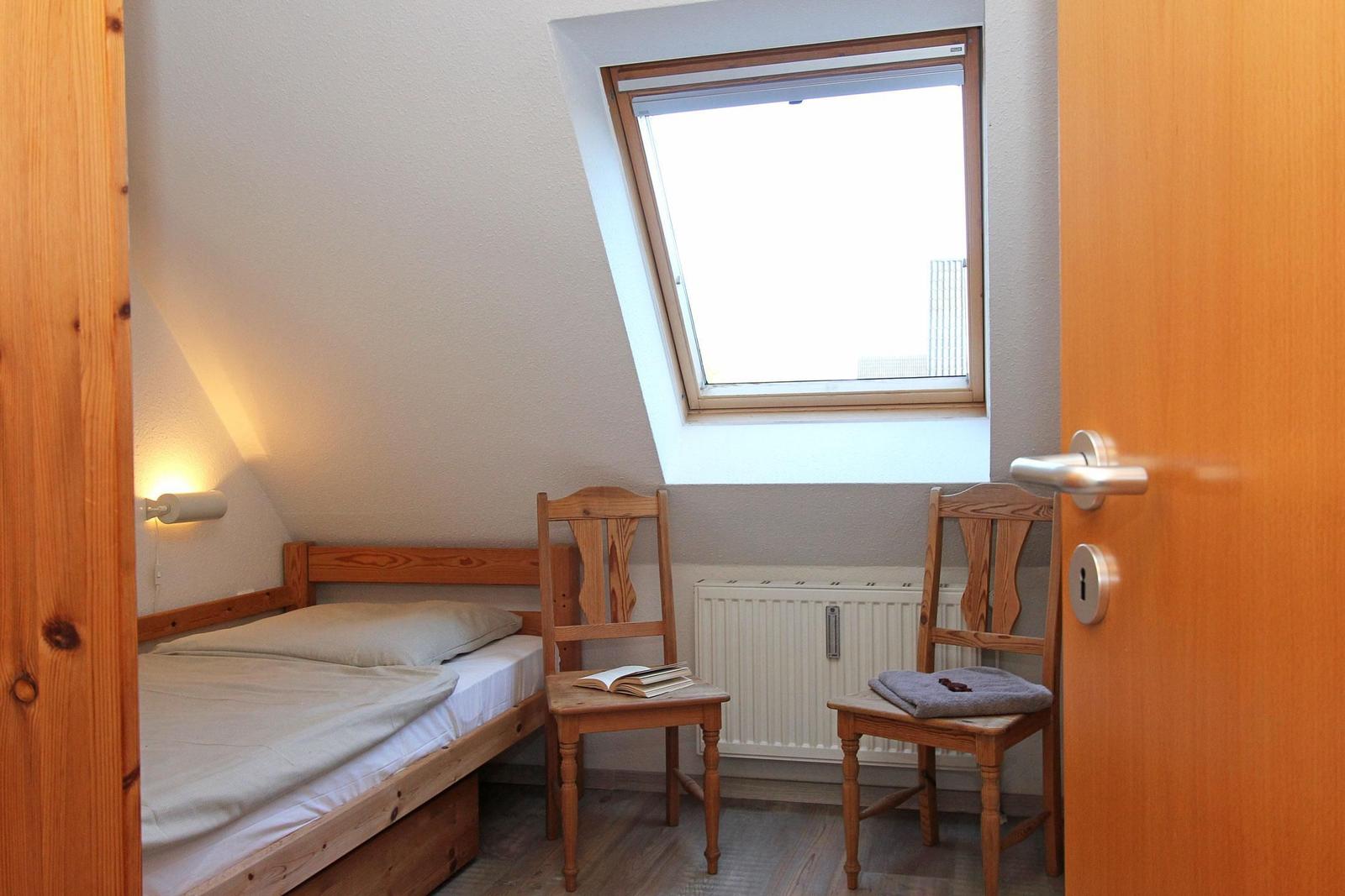Ein Schlafzimmer mit Dachschrägen, einem Bett, zwei Stühlen und einem Dachfenster.
