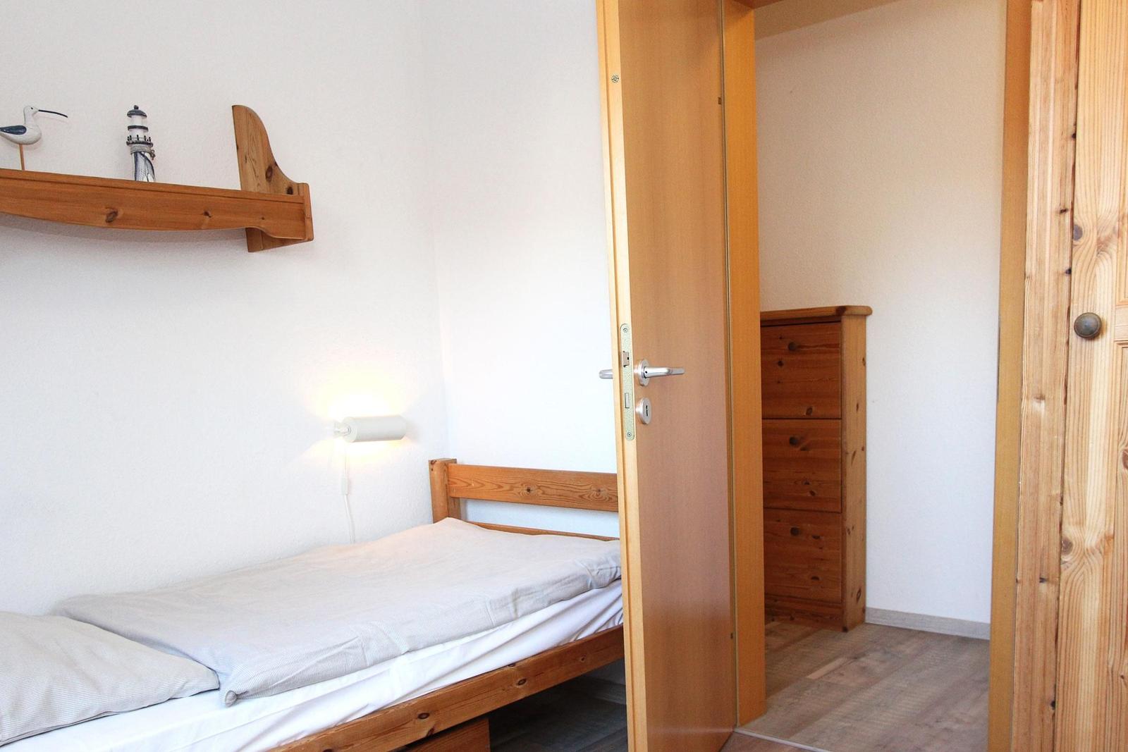 Schlafzimmer mit Holzbett, Wandregal und Tür zum Ankleidebereich.