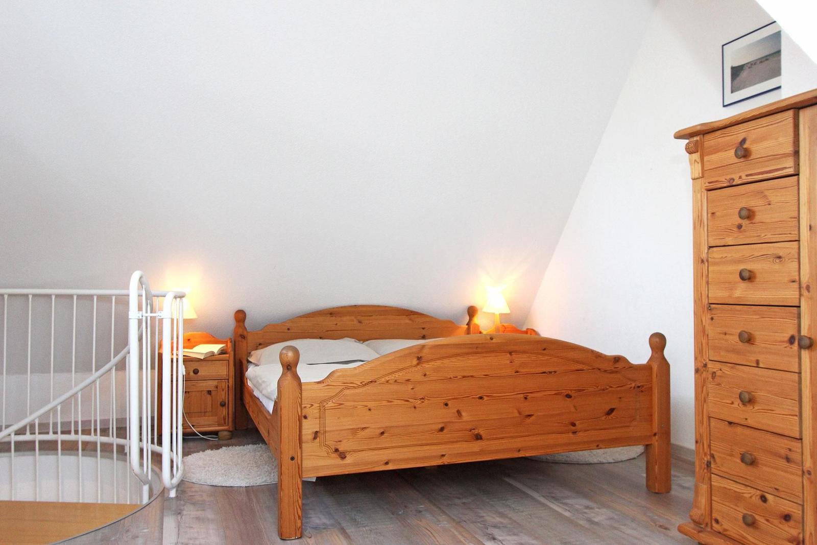 Schlafzimmer mit Holzbett, Kleiderschrank und Nachttisch unter schrägen Wänden.
