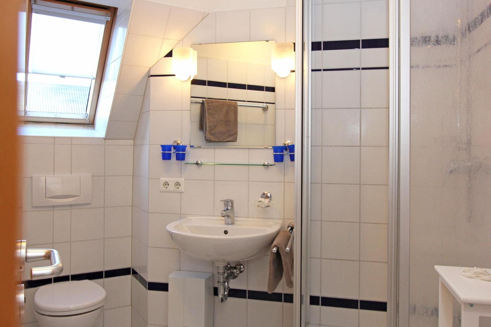 Badezimmer mit Dusche, Waschbecken und Toilette. Weiße Fliesen mit dunklen Streifen.