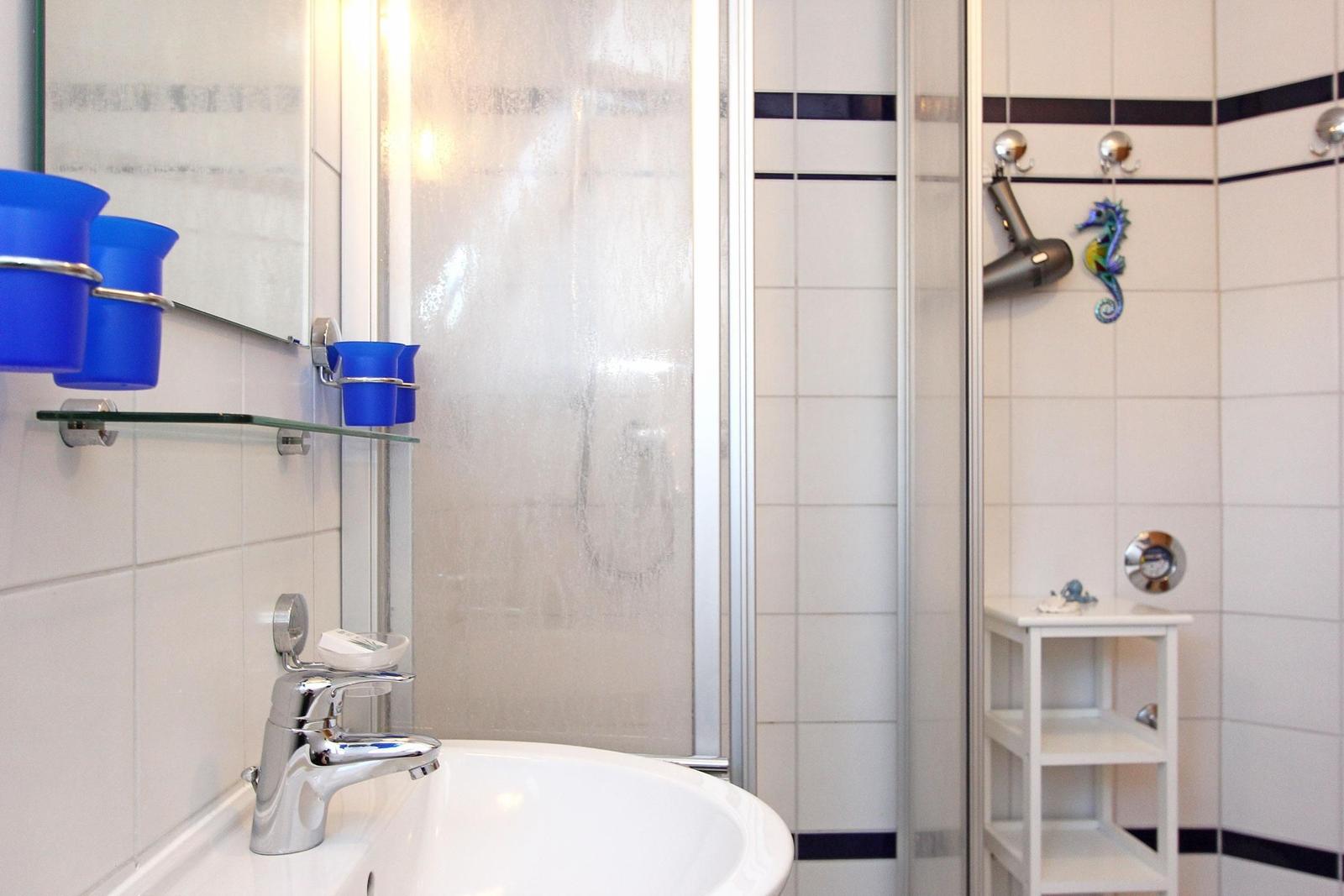 Bad mit Dusche, Waschbecken und blauen Behältern.