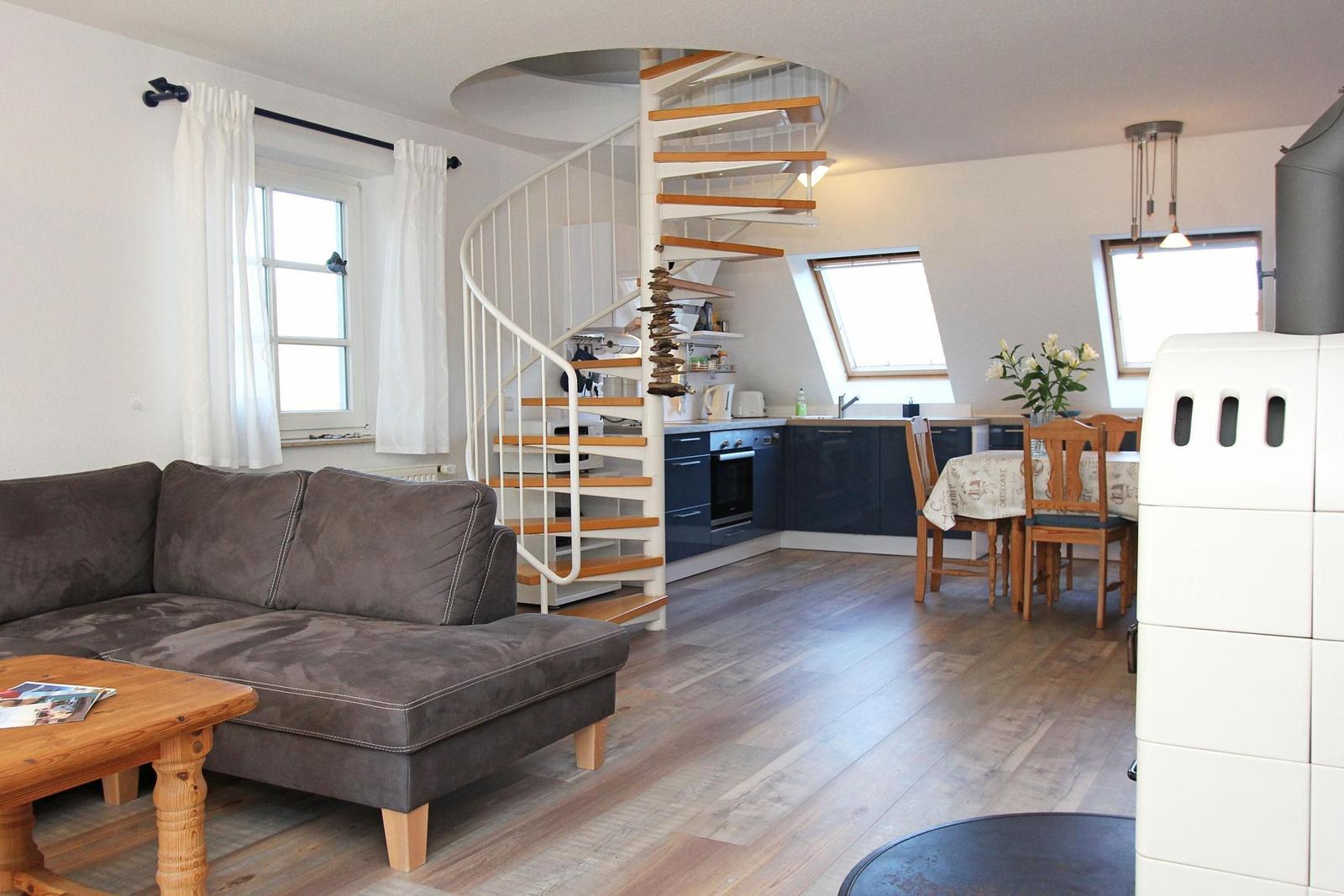 Wohnbereich mit Sofa, Küchenbereich und Tisch mit Stühlen. Eine Wendeltreppe führt nach oben.